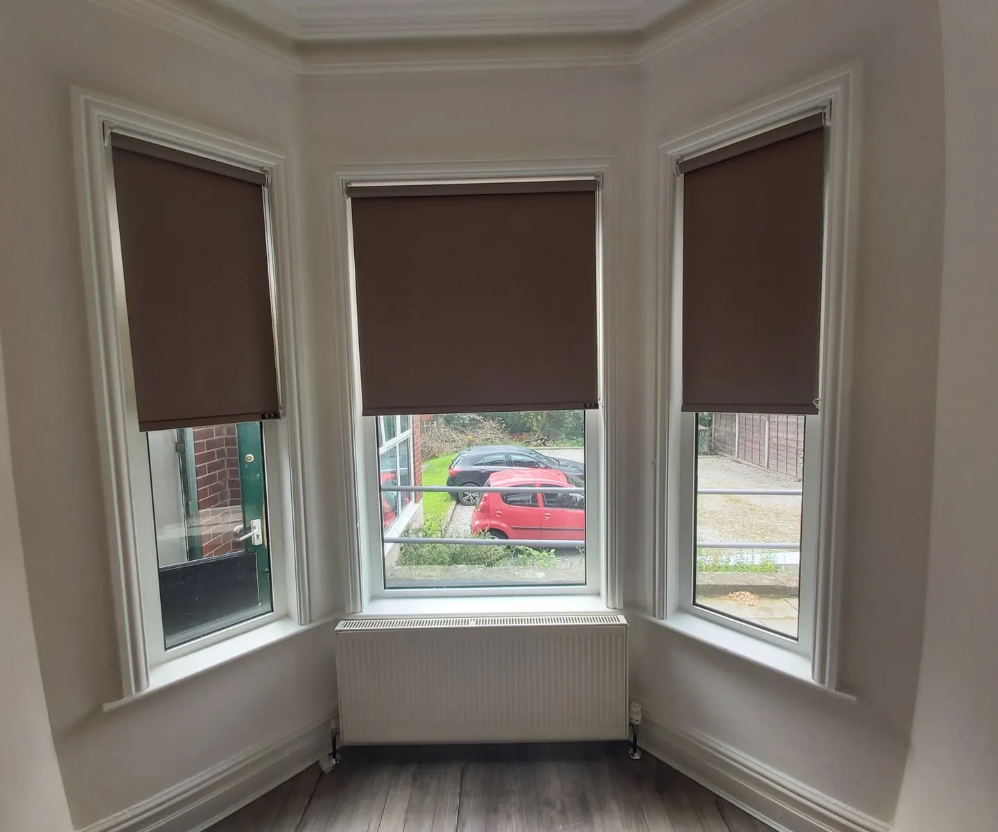 Grey roller blinds across a wide bay window with a radiator below, seen from the room