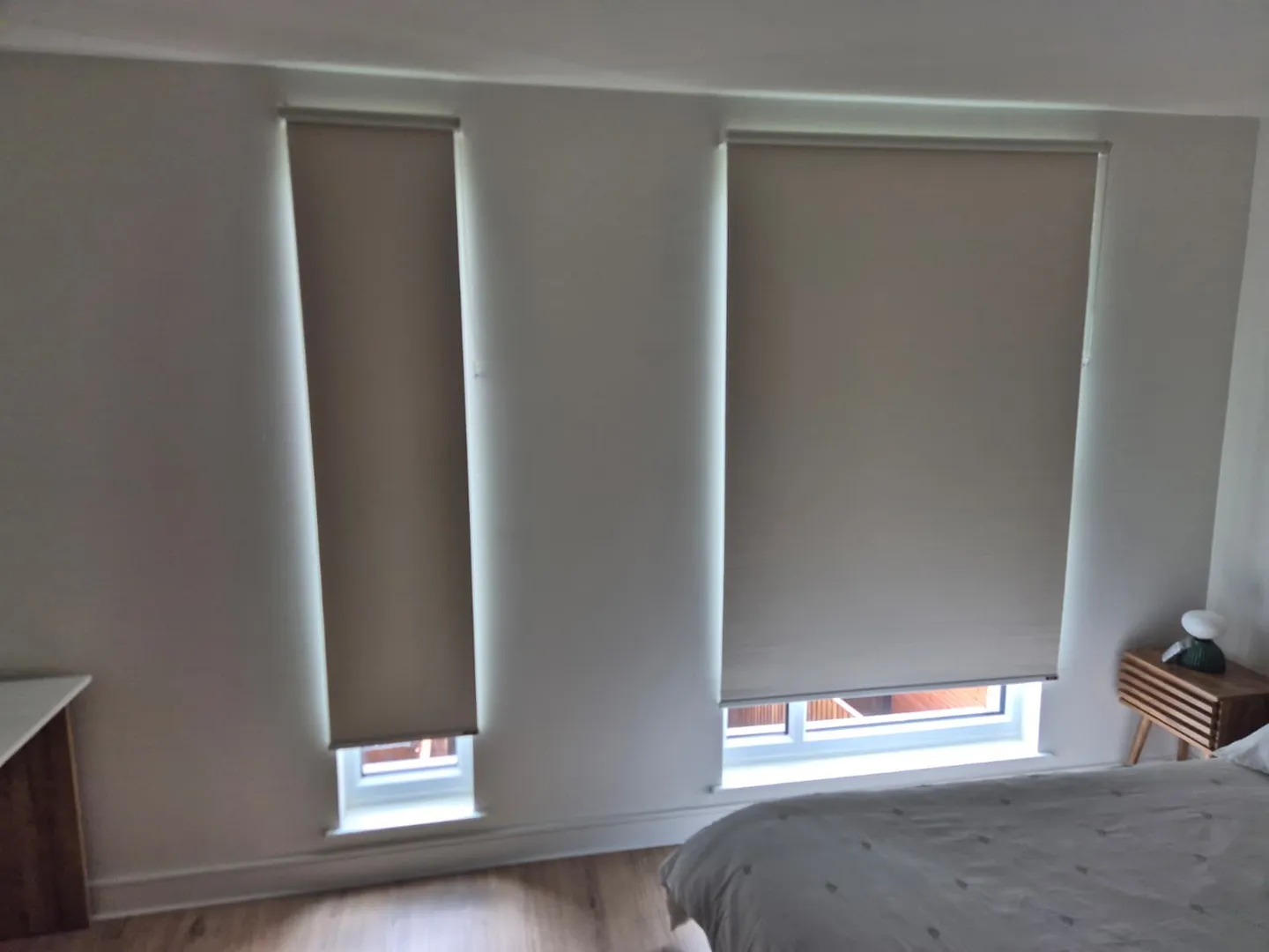 Cream roller blinds on a tall narrow window and a wider window in a white bedroom