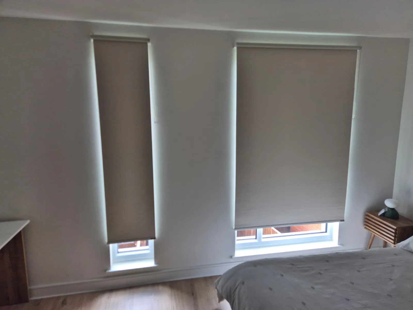 Cream roller blinds on a tall narrow window and a wider window in a white bedroom