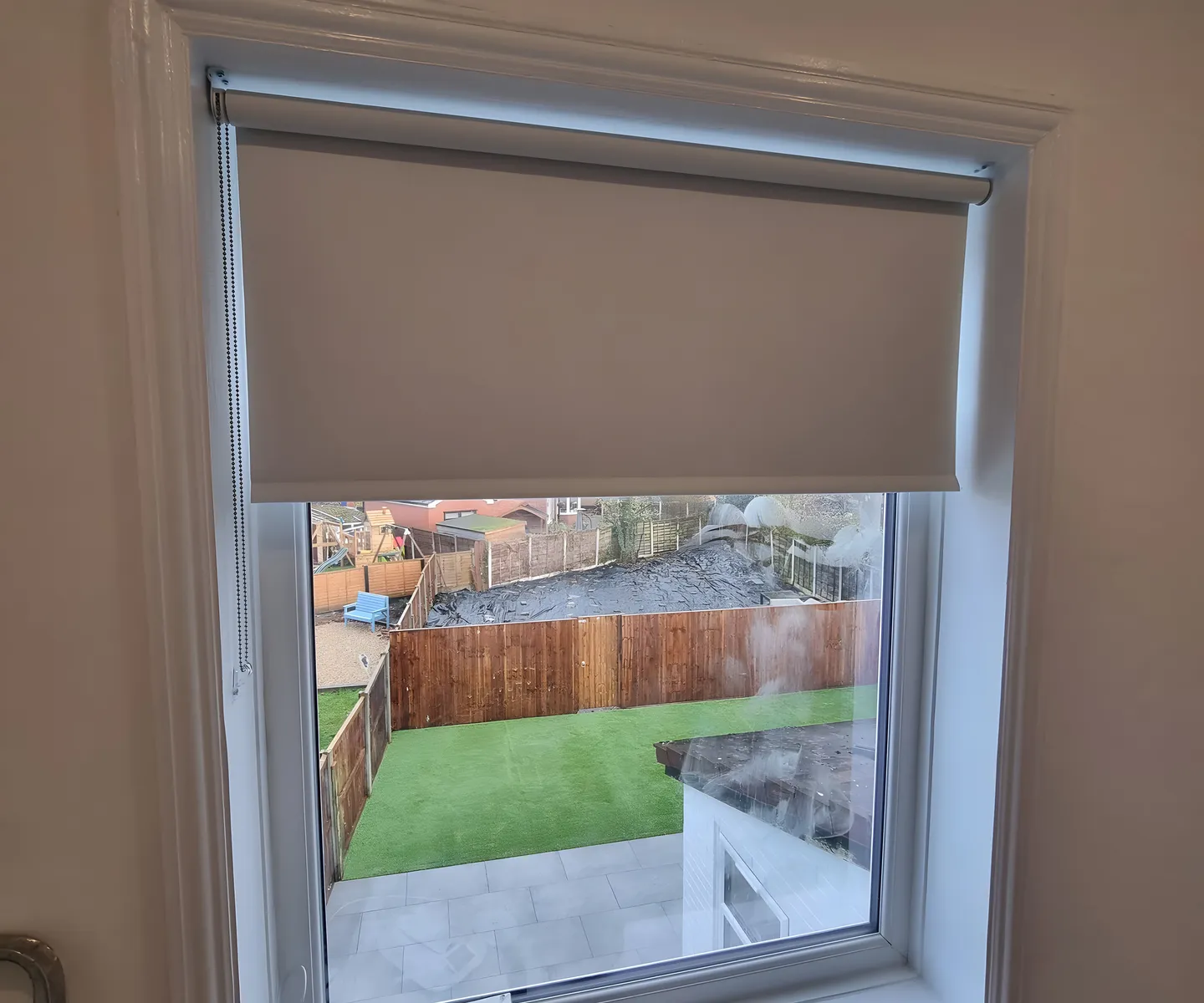 Dark blackout roller blind half lowered on a landing window overlooking a garden