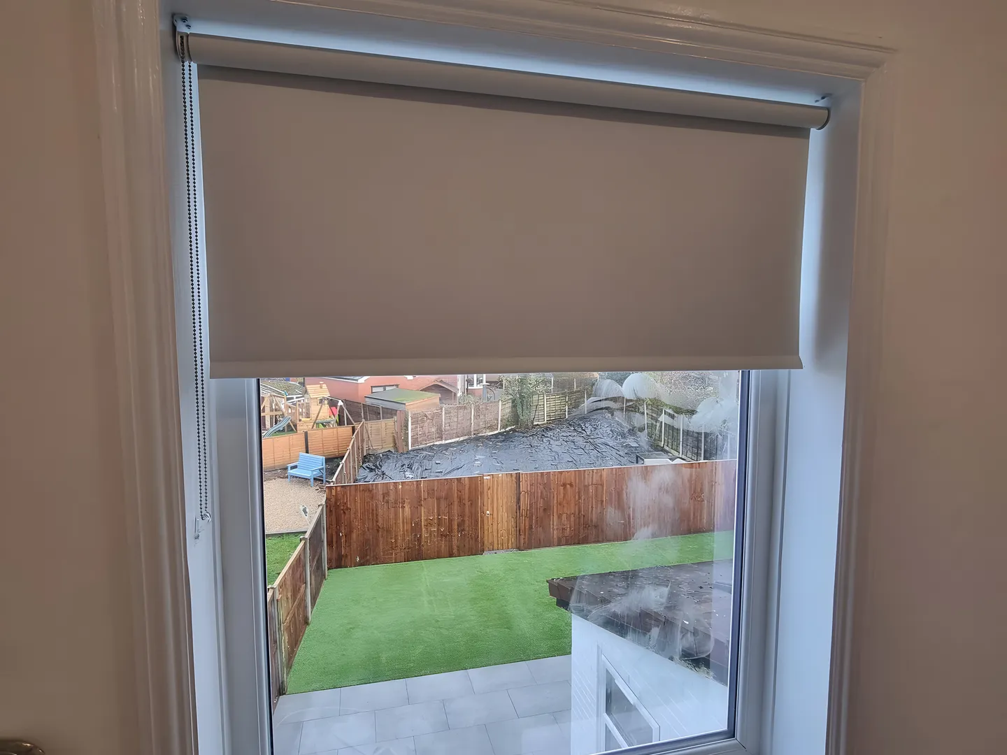 Dark blackout roller blind half lowered on a landing window overlooking a garden