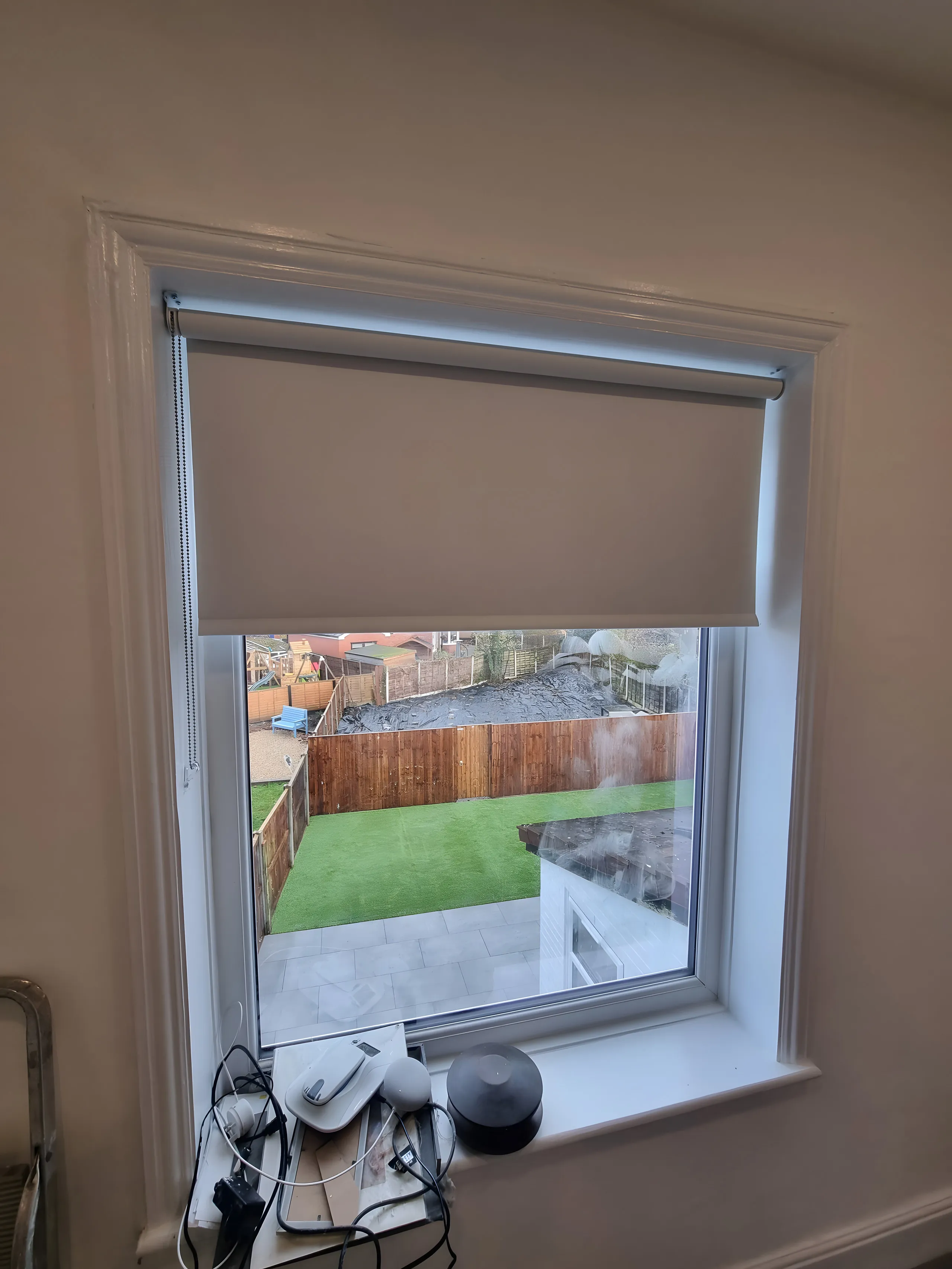 Dark blackout roller blind half lowered on a landing window overlooking a garden