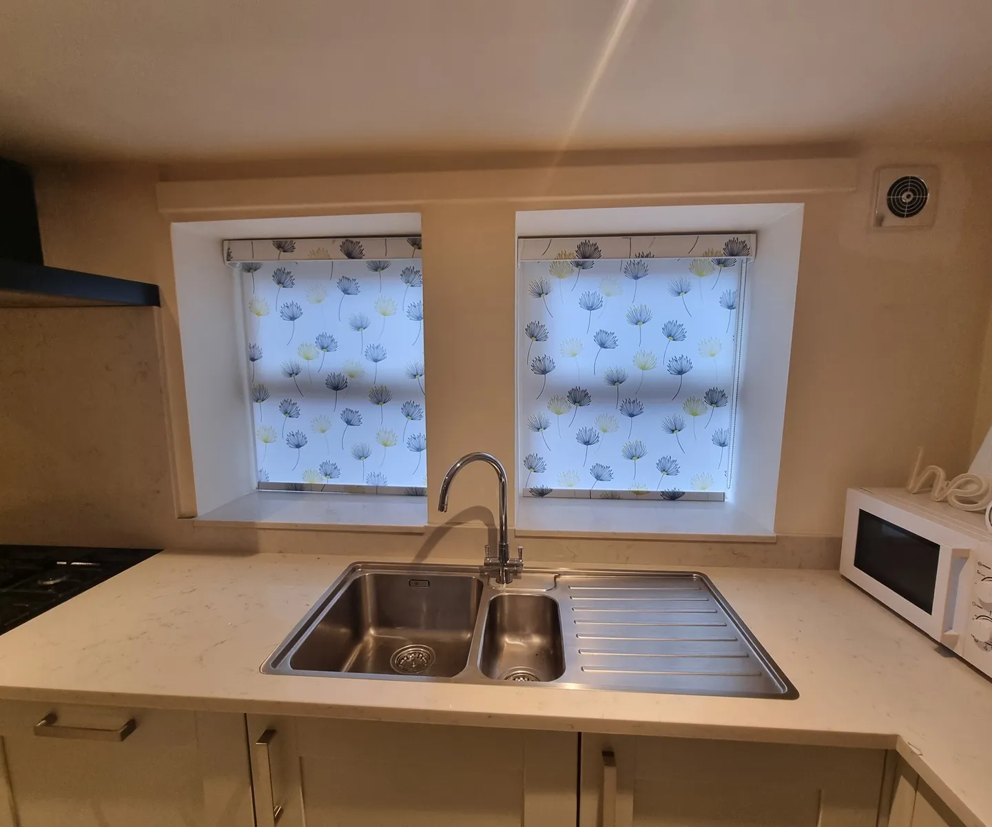 Patterned roller blinds over a double kitchen window above the sink