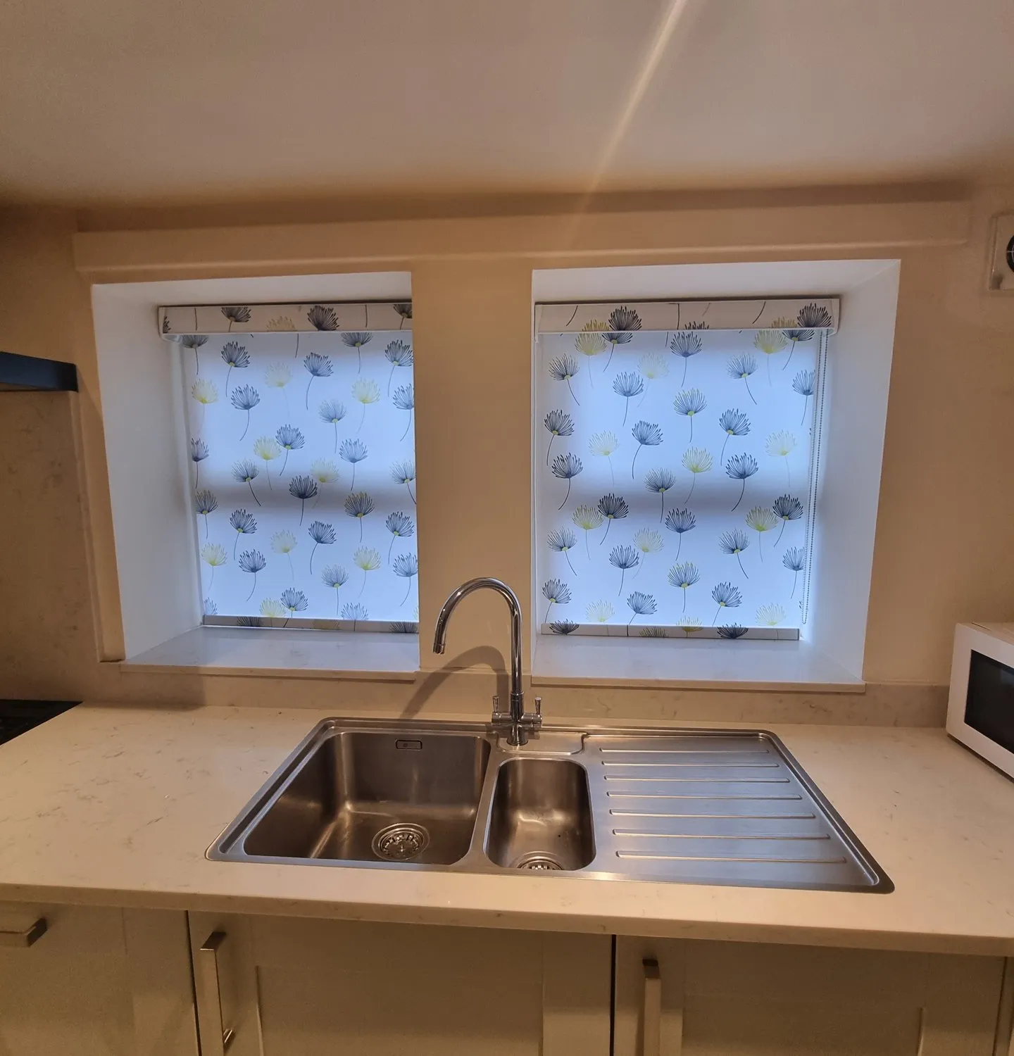 Patterned roller blinds over a double kitchen window above the sink
