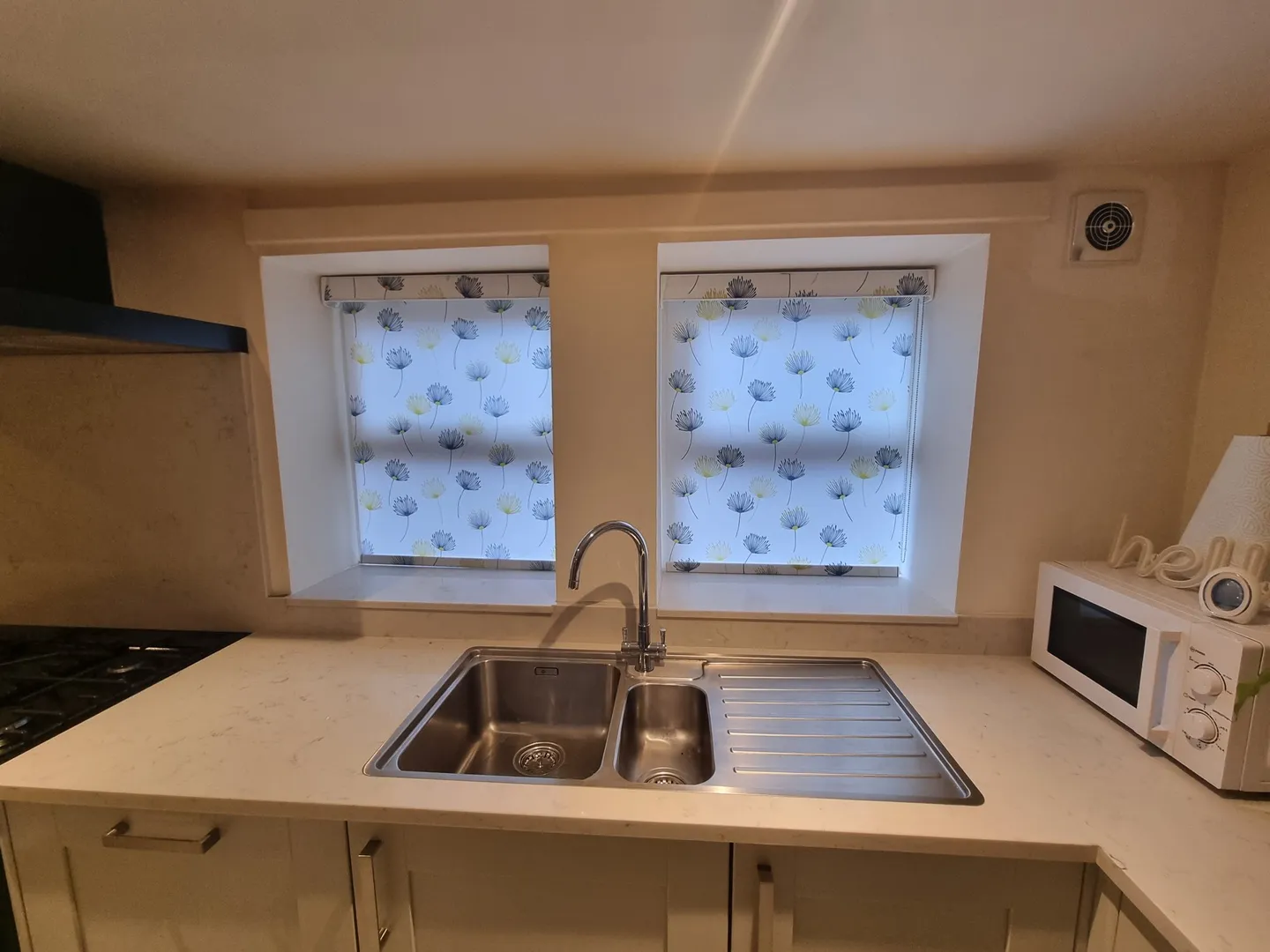 Patterned roller blinds over a double kitchen window above the sink