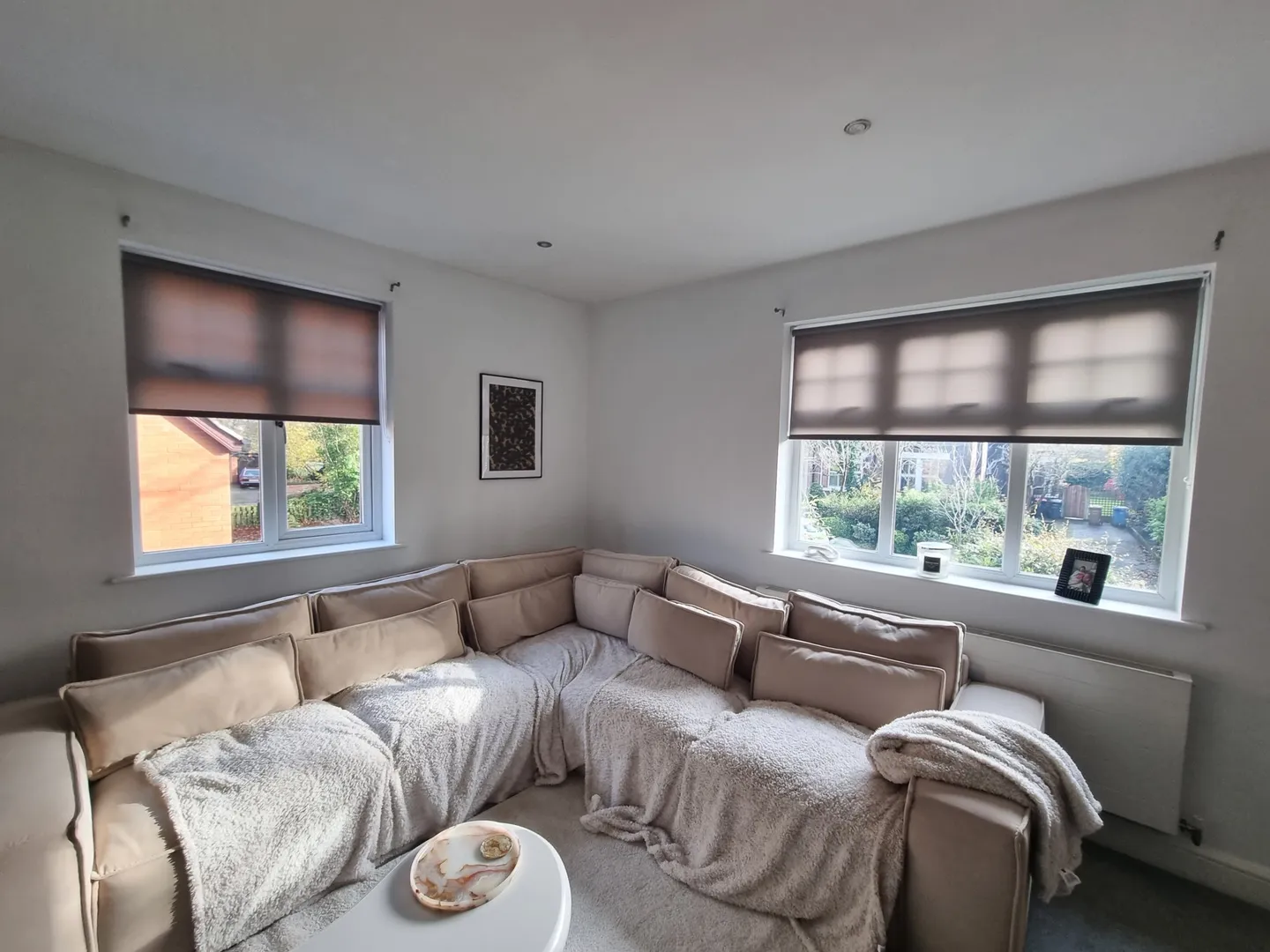 Two patterned roller blinds in a living room above a large corner sofa