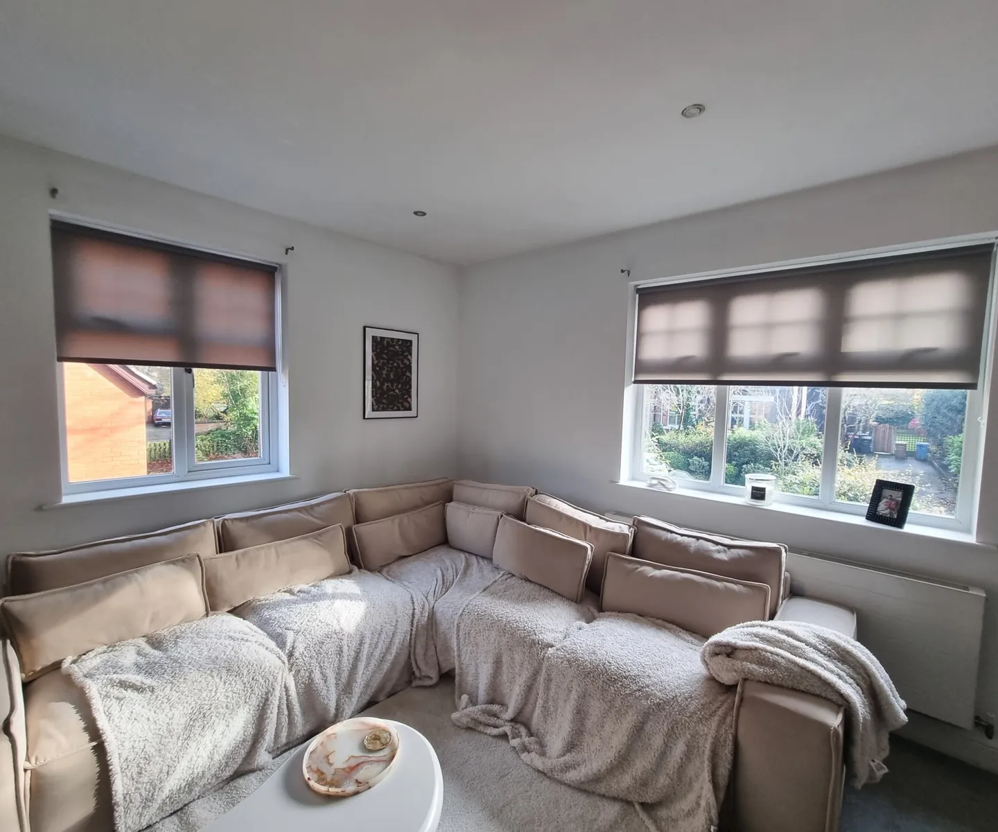 Two patterned roller blinds in a living room above a large corner sofa