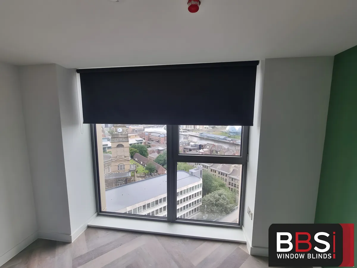 Dark blackout roller blind half lowered over a bedroom window