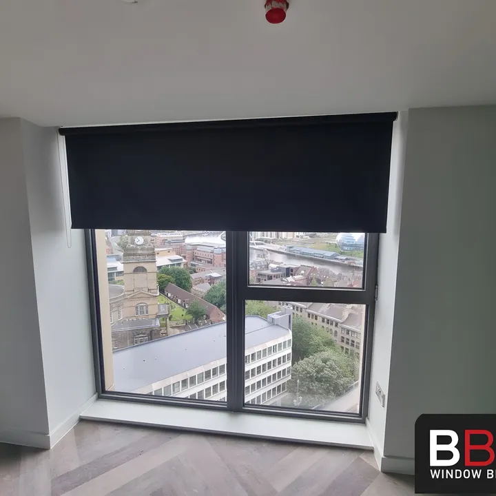 Dark blackout roller blind half lowered over a bedroom window