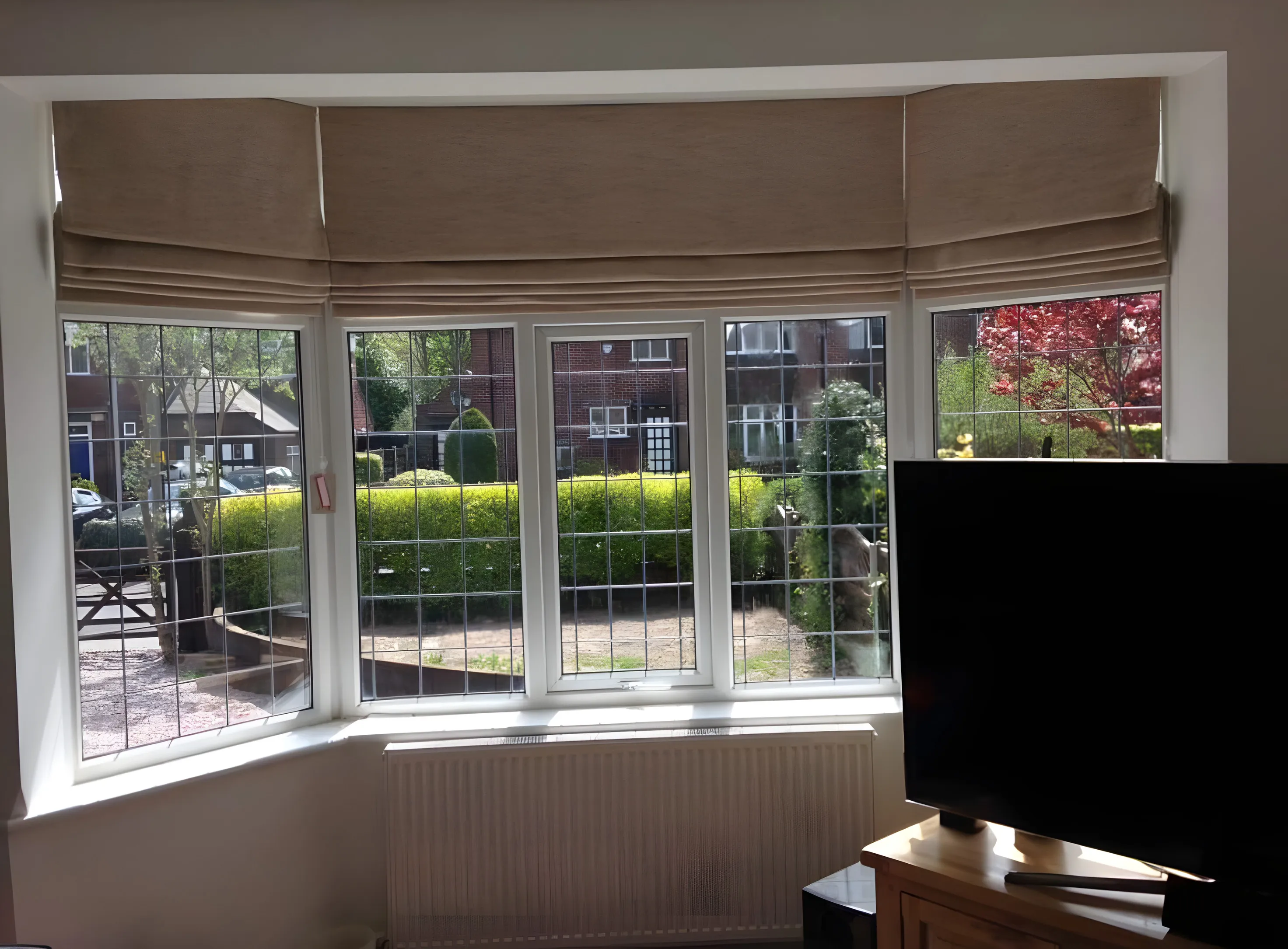 Neutral Roman blinds fitted to each pane of a leaded bay window above a radiator