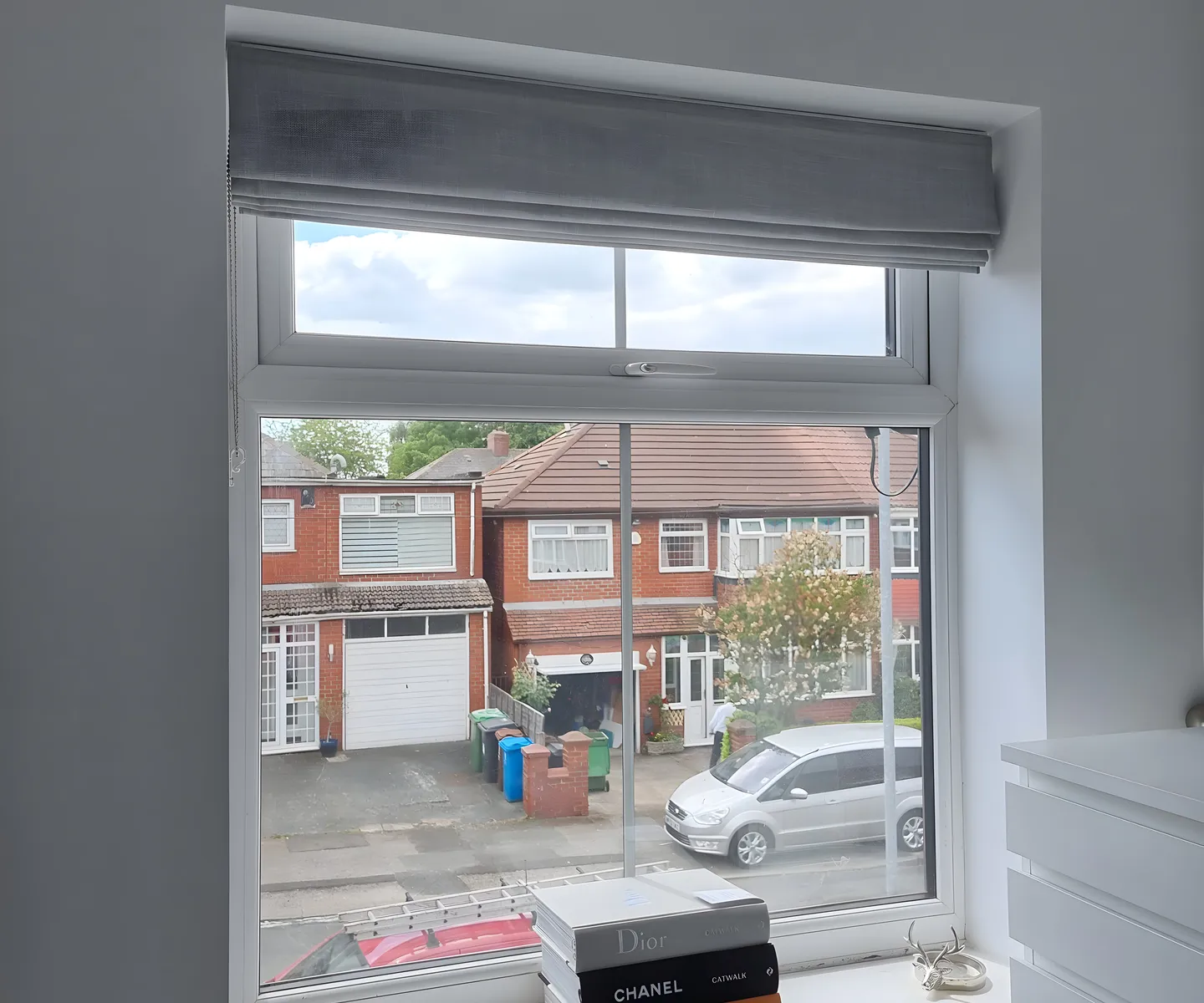 Grey Roman blind lowered at a bedroom window overlooking the street