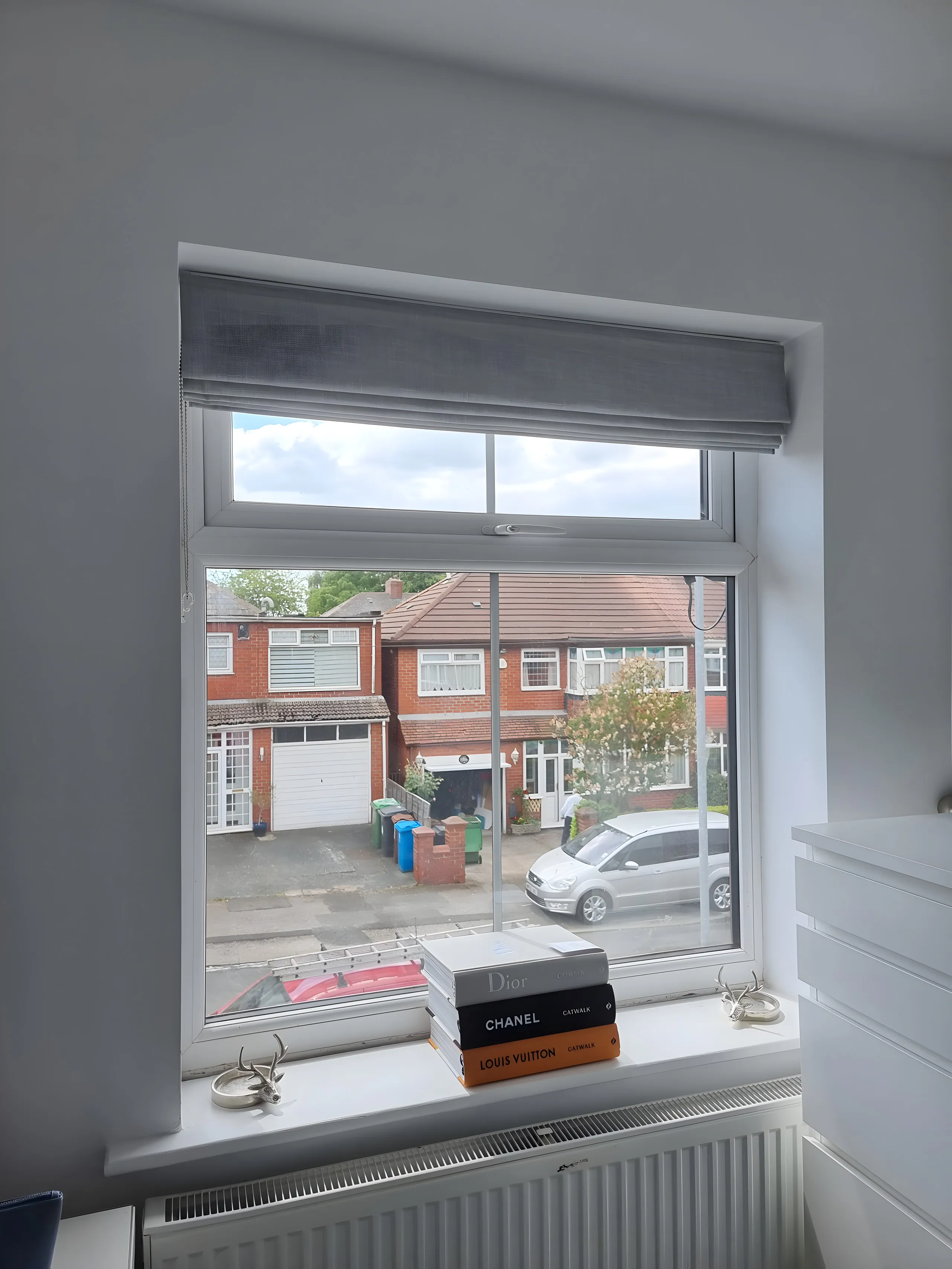 Grey Roman blind lowered at a bedroom window overlooking the street