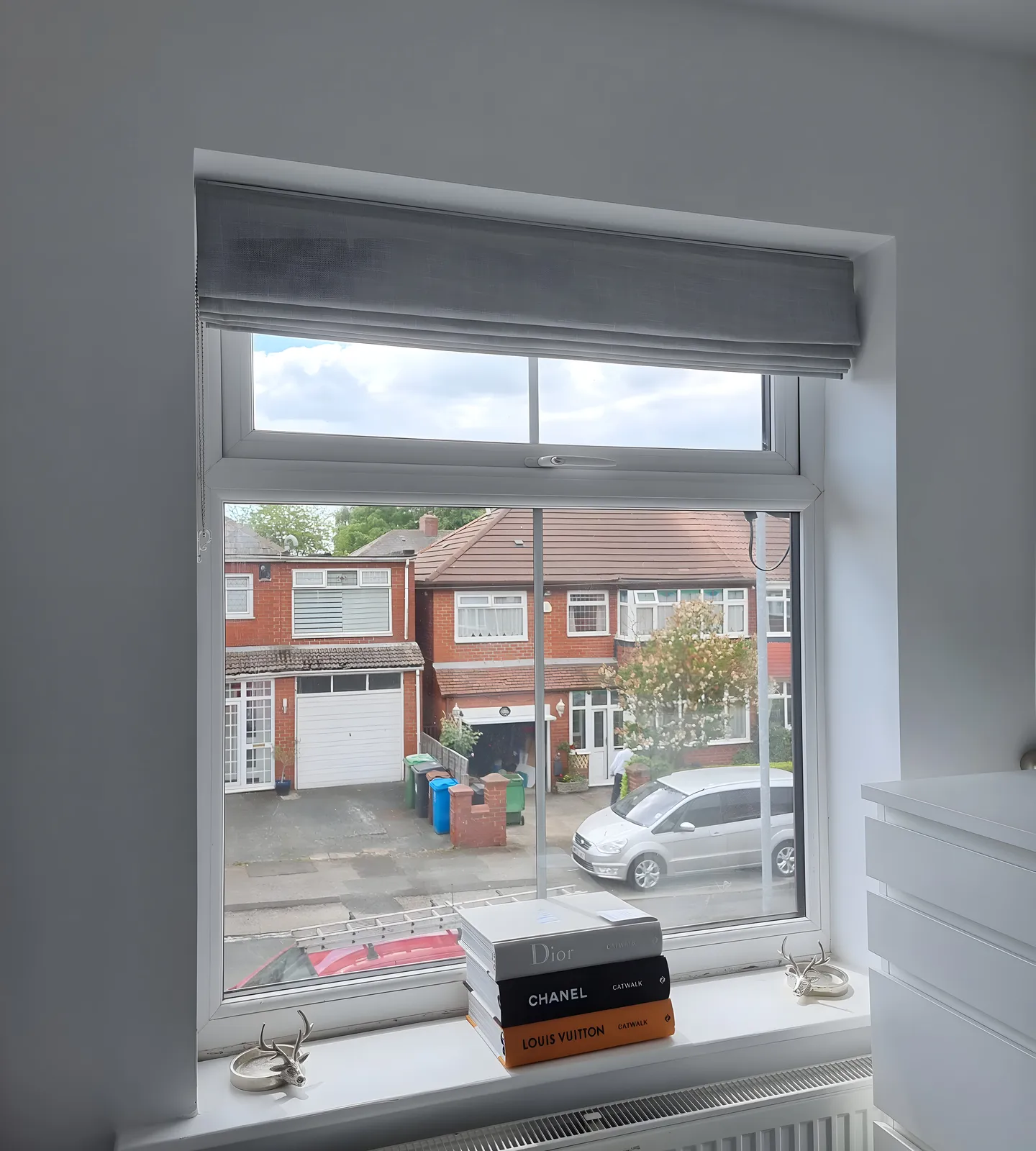 Grey Roman blind lowered at a bedroom window overlooking the street