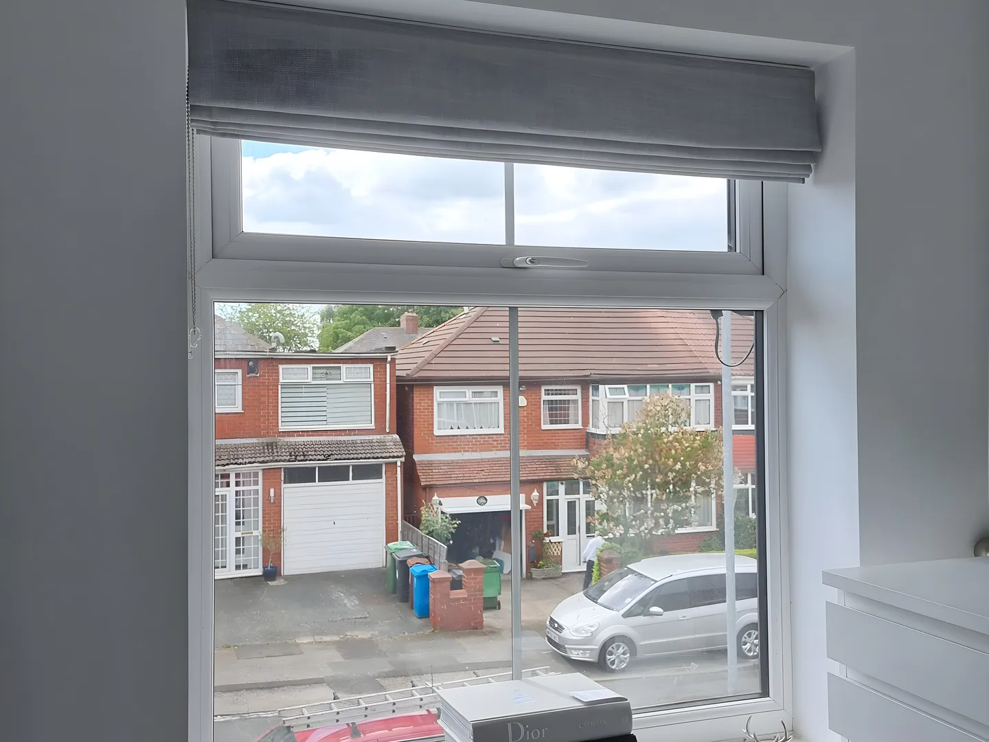 Grey Roman blind lowered at a bedroom window overlooking the street