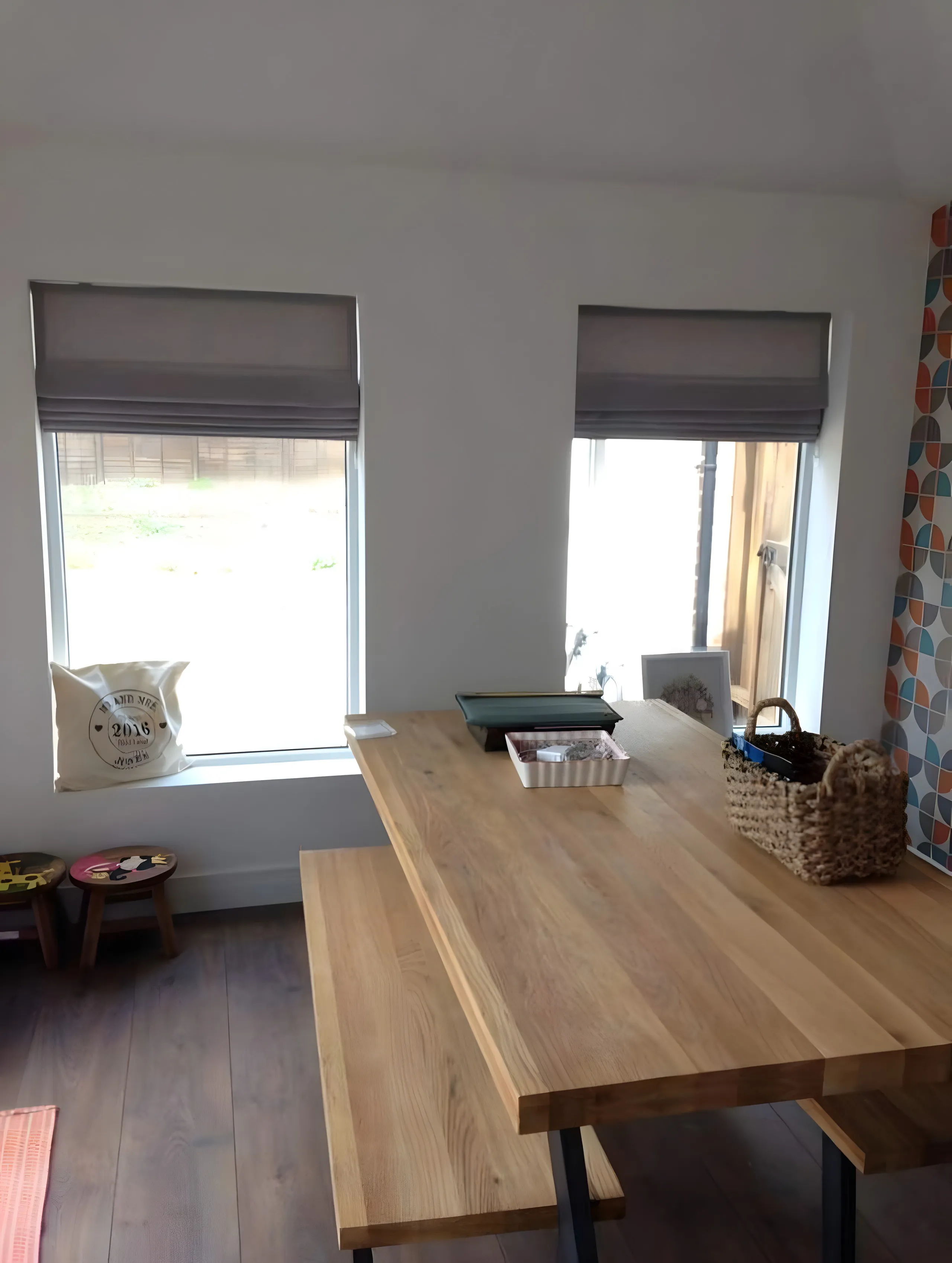 Pair of grey Roman blinds at the windows of a kitchen diner with an oak table