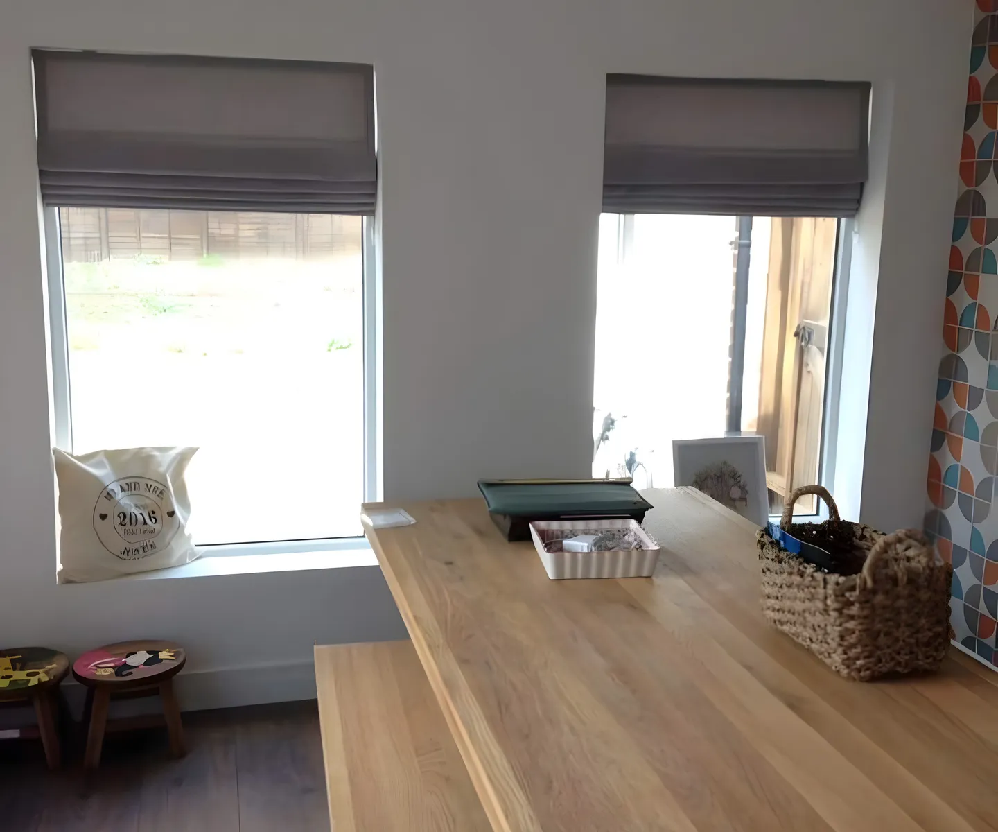 Pair of grey Roman blinds at the windows of a kitchen diner with an oak table