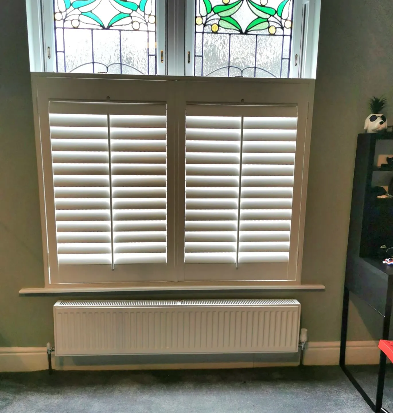 White café style shutters on the lower half of a period window, the original stained glass lights left clear above