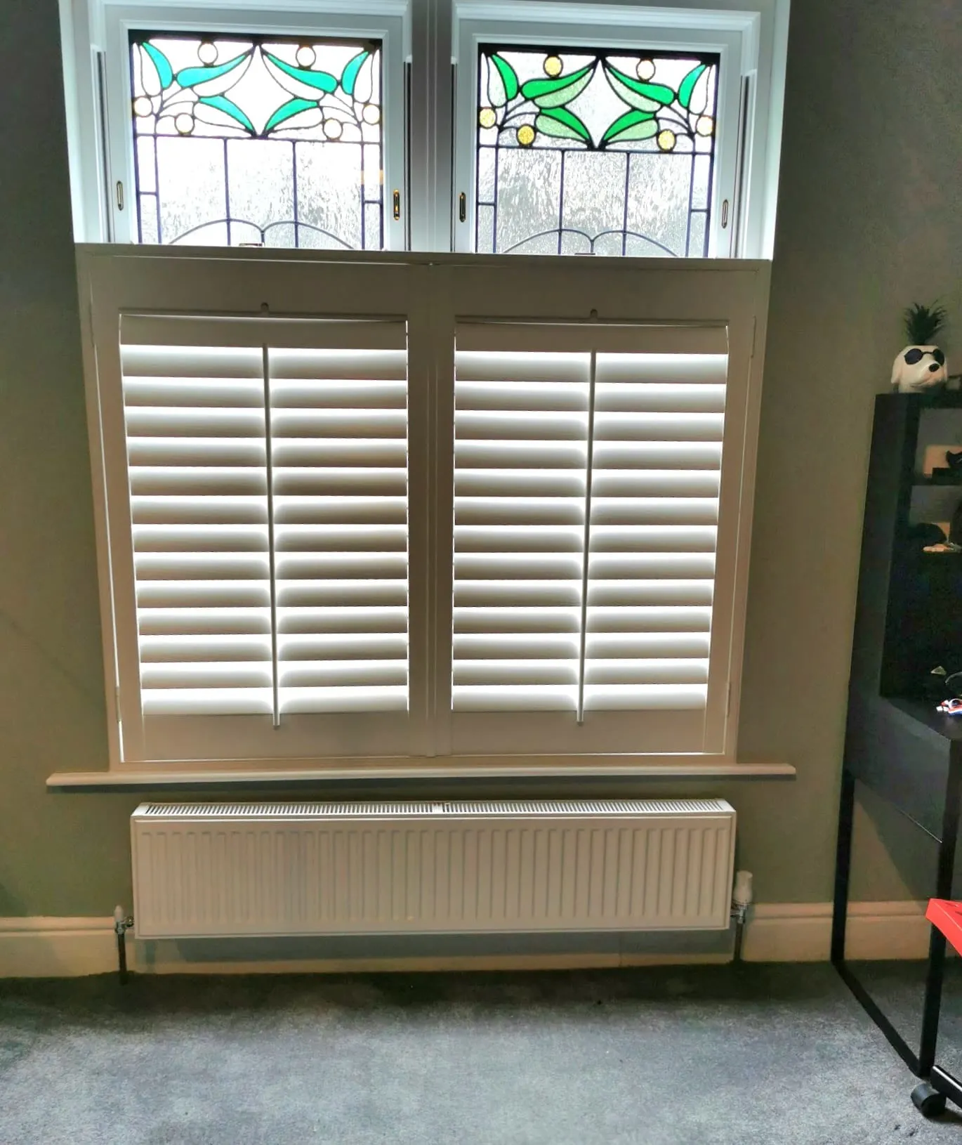 White café style shutters on the lower half of a period window, with the original stained glass lights left clear above
