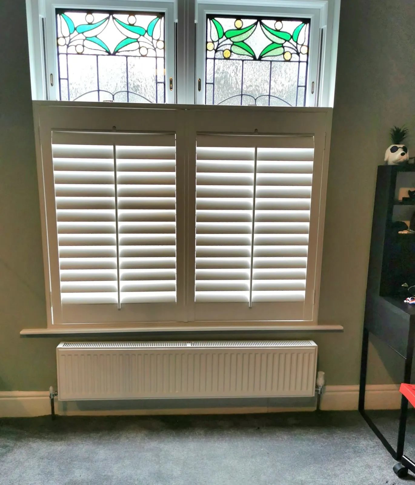 White café style shutters on the lower half of a period window, with the original stained glass lights left clear above