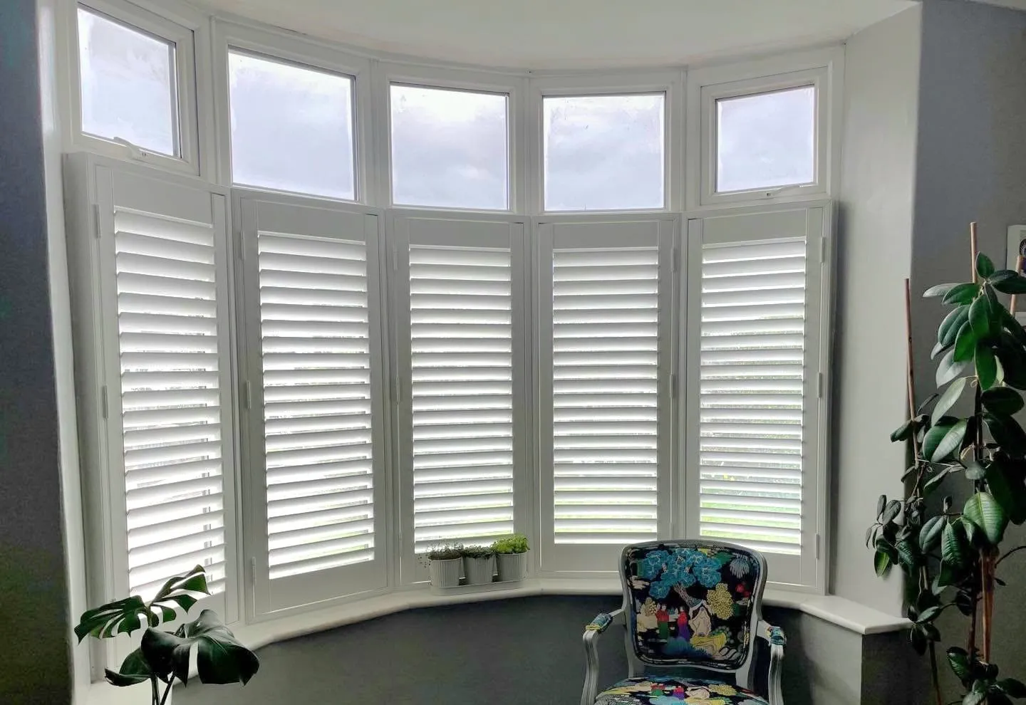 White café style shutters following the curve of a dining room bay, with plants along the sill