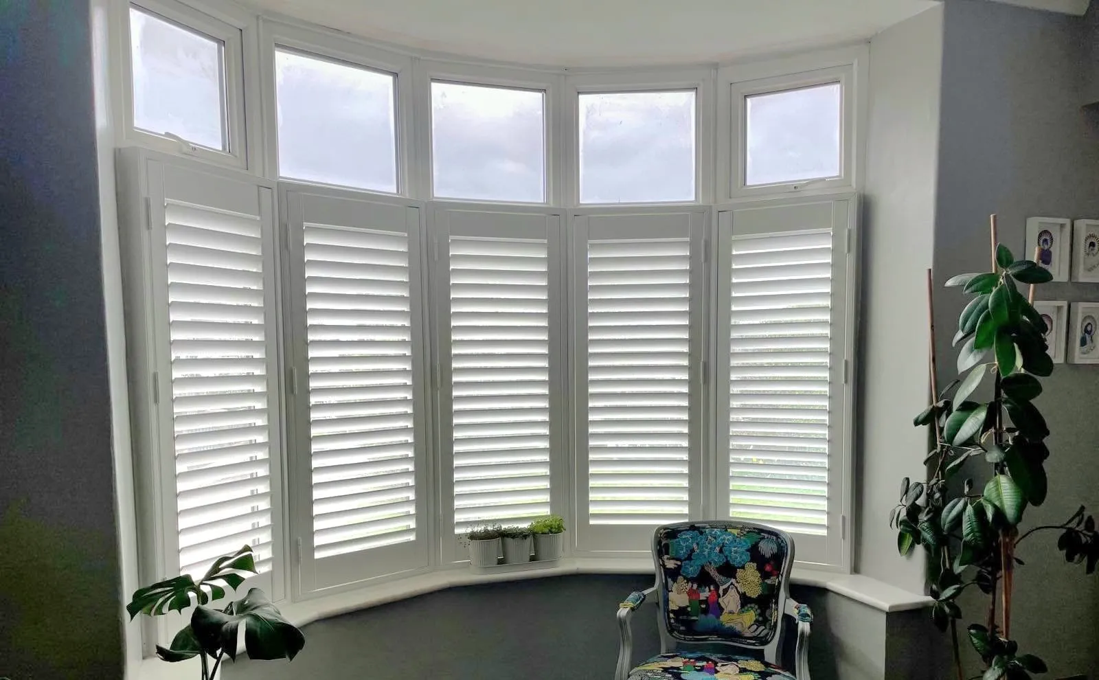 White café style shutters following the curve of a dining room bay, with plants along the sill