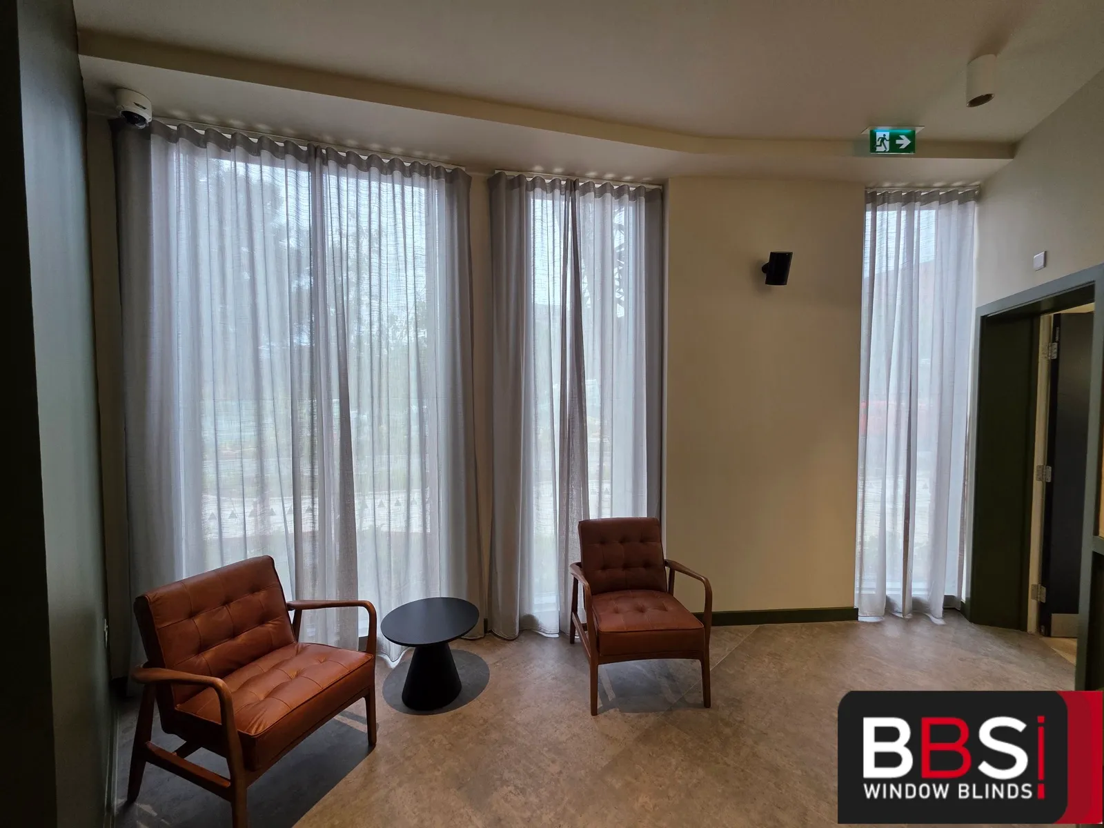 Reception seating area at Skinner Street with full height wave sheers on the corner glazing behind two leather armchairs