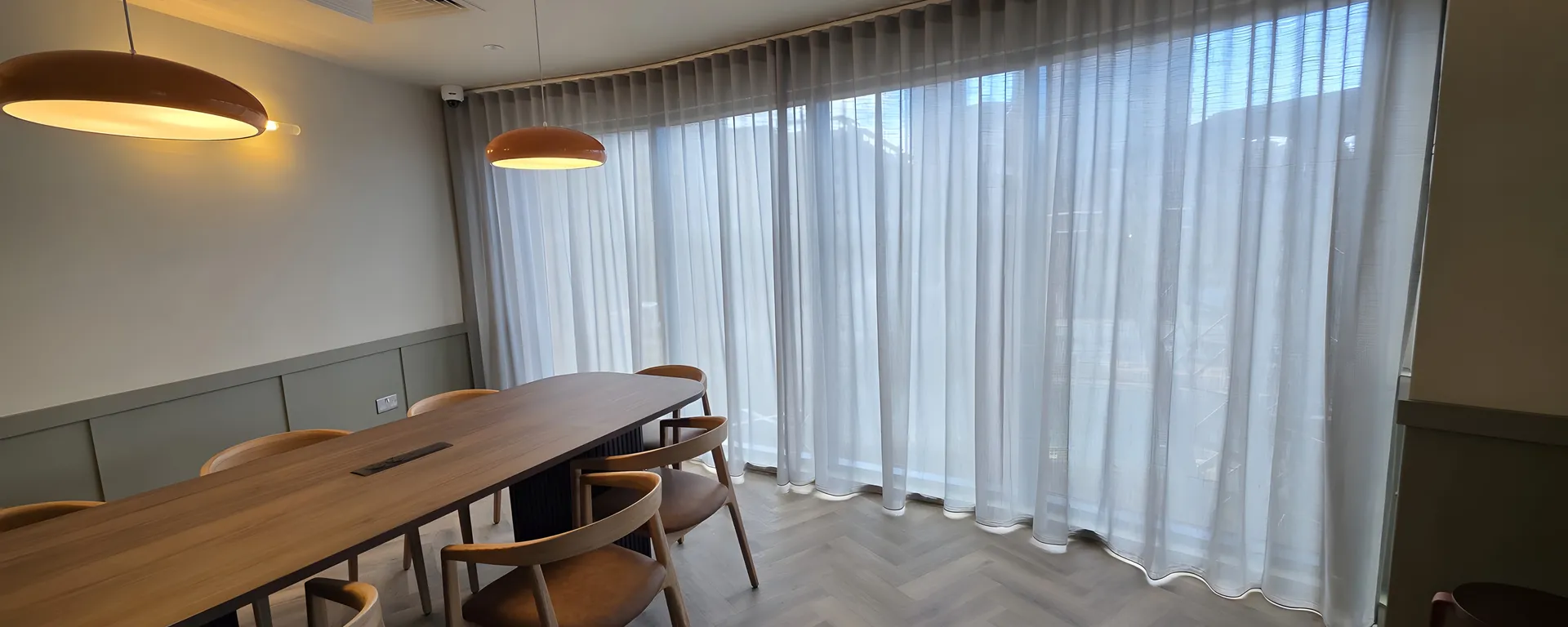 Wave sheer curtains on a bend-formed curved track wrapping the corner glazing of a co-working meeting room at Skinner Street