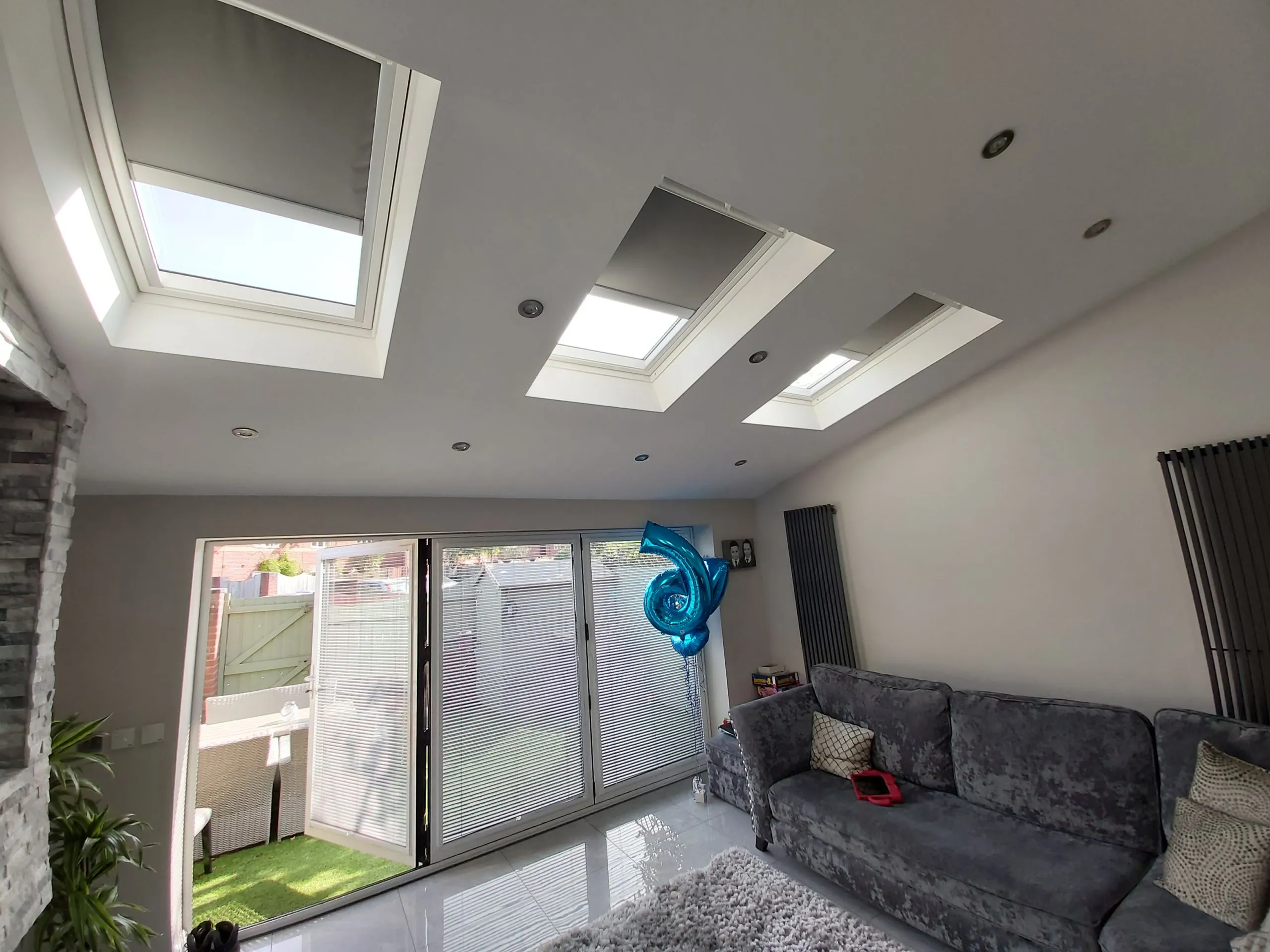 Three skylight blinds fitted to the roof of a single-storey extension with a grey sofa and garden doors