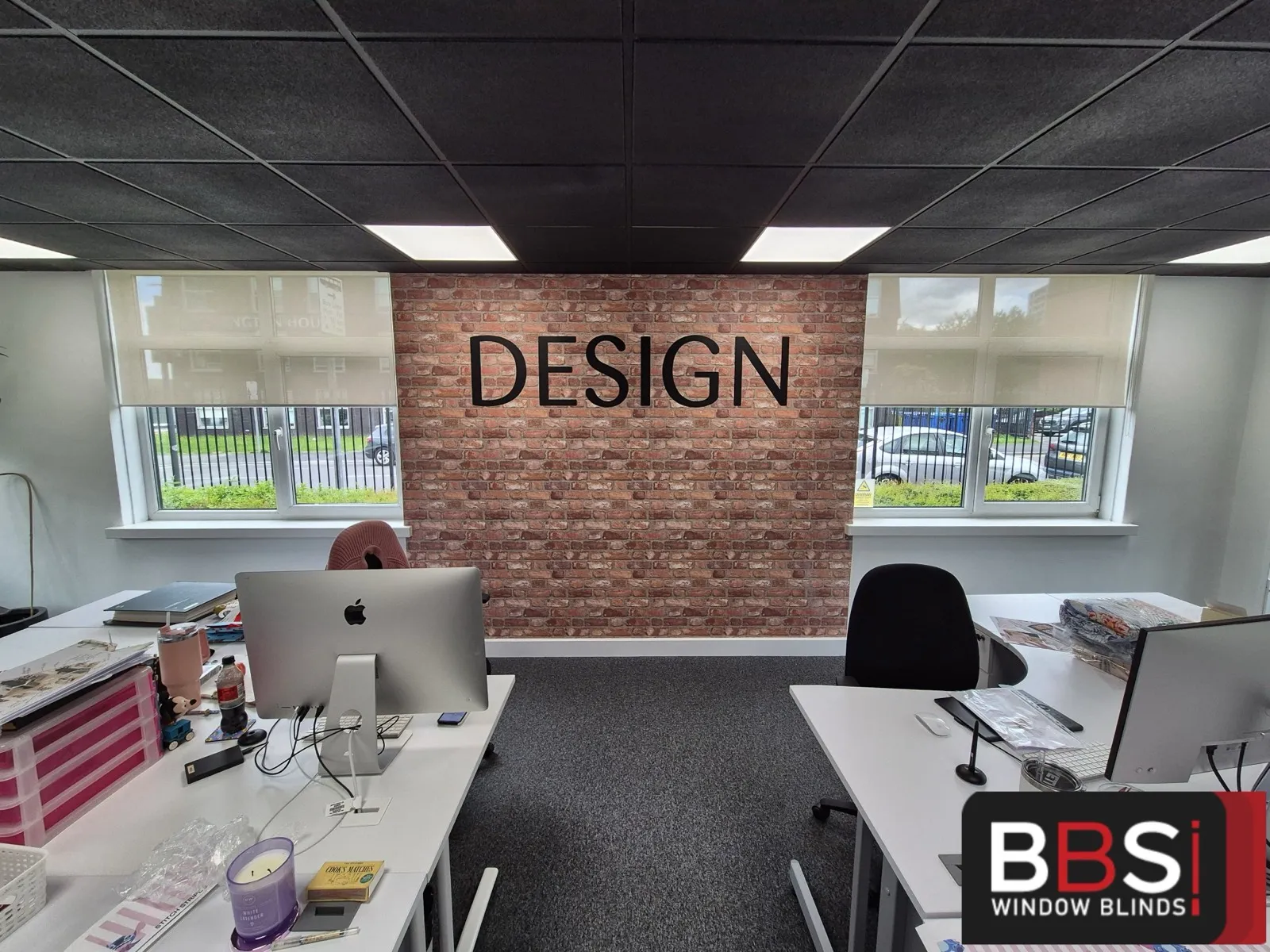 Design studio desks with matching screen fabric roller blinds on the windows either side of a brick feature wall