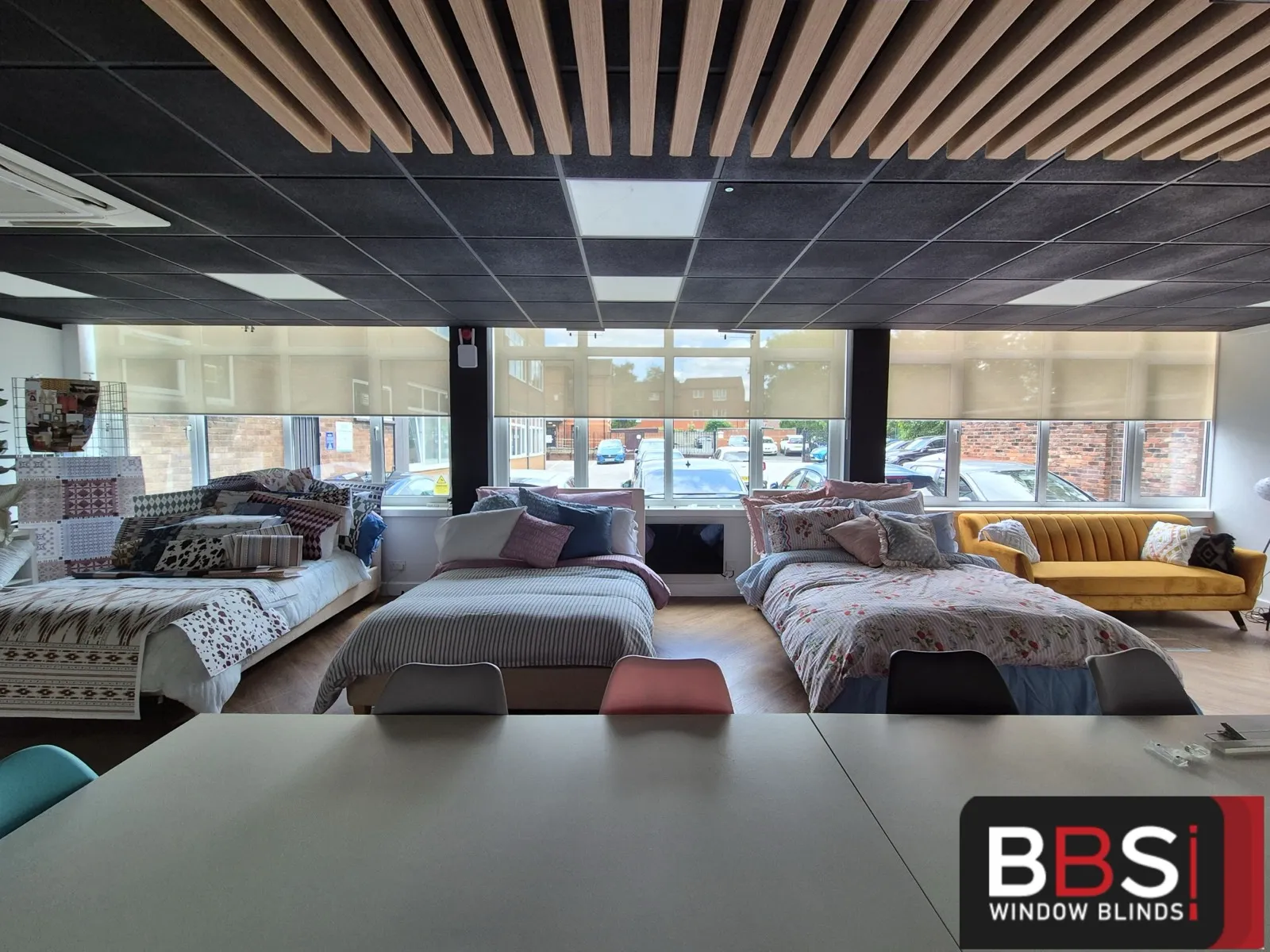 Bedding showroom with made up display beds and screen fabric roller blinds across the full glazed shopfront behind them