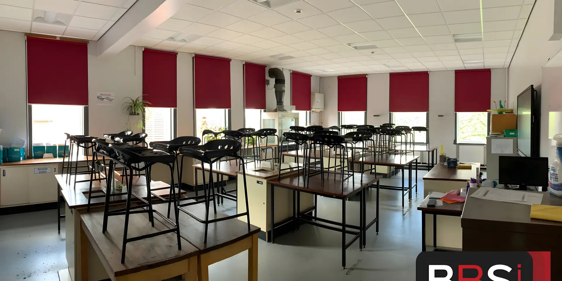 Burgundy roller blinds fitted by BBS across a classroom at Stockport School, with full-size lab stools stacked on the desks