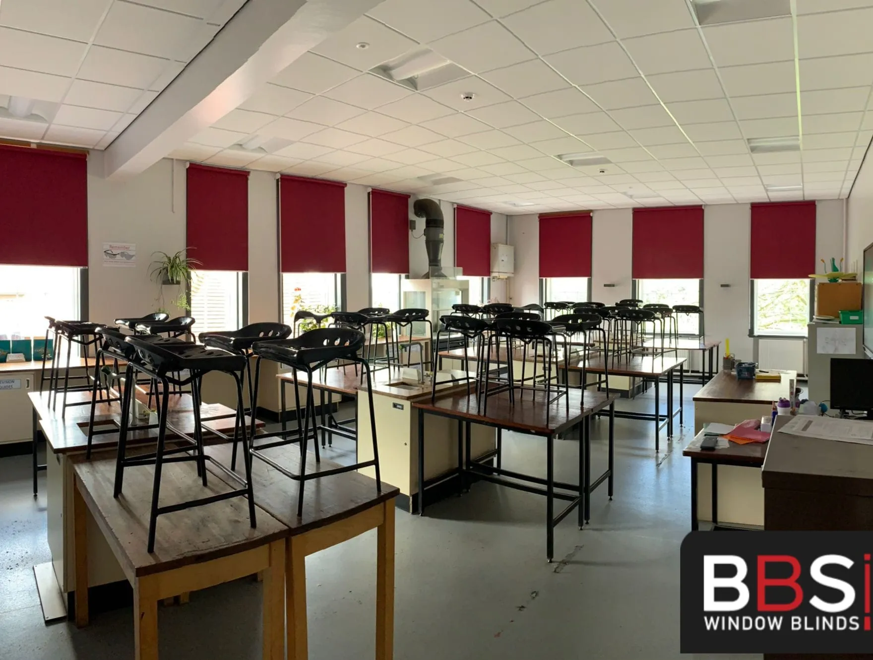Burgundy roller blinds across tall classroom windows at Stockport School, with chairs stacked on the desks