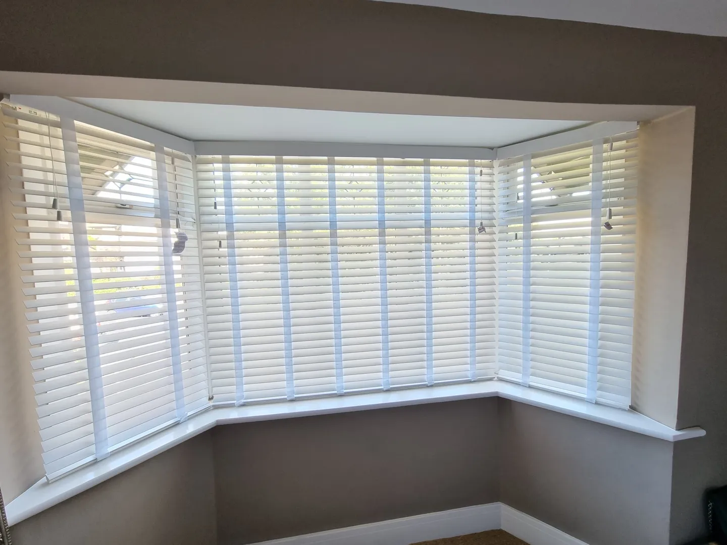 White Venetian blinds across a living room bay window behind a grey sofa