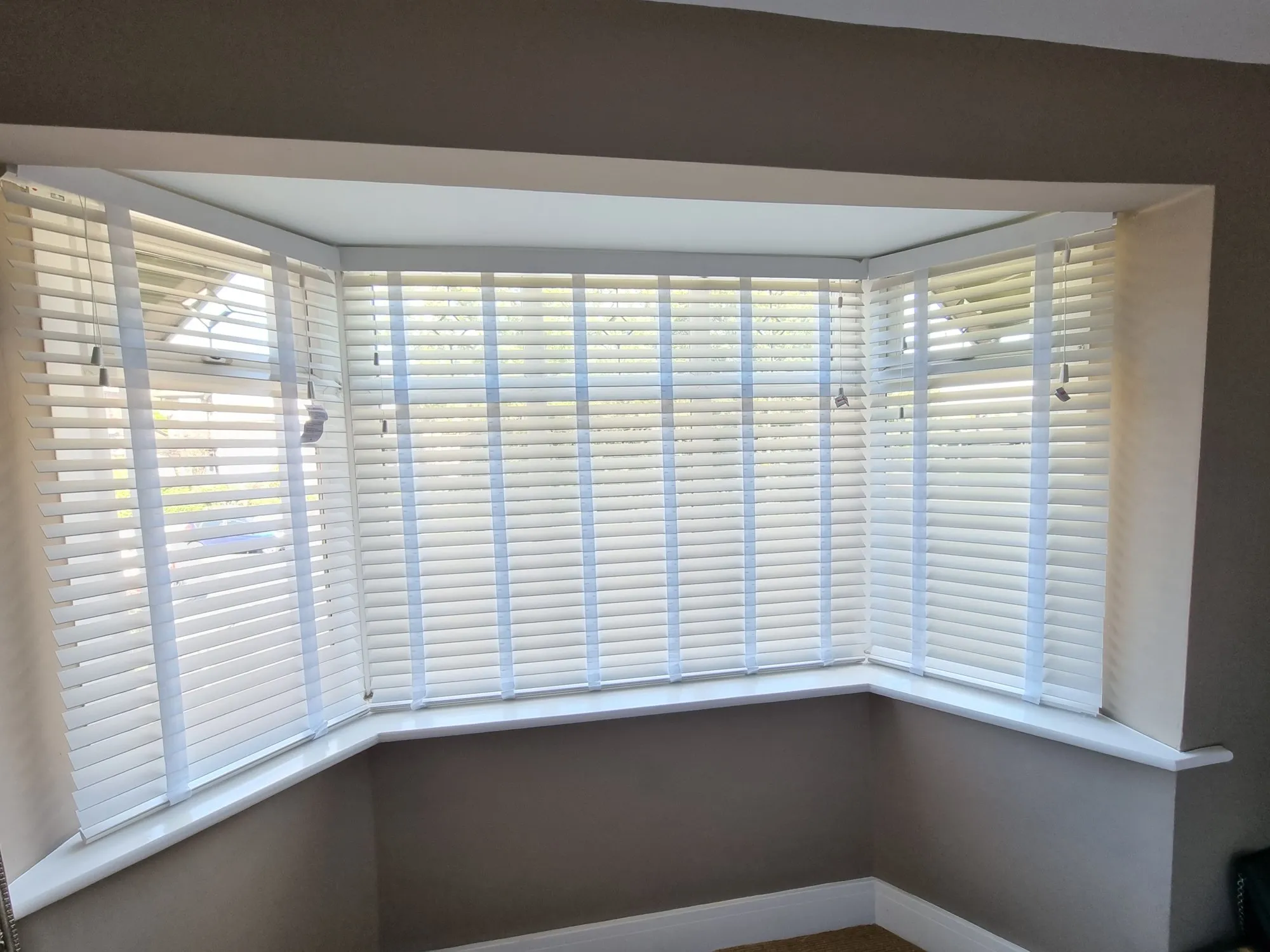 White Venetian blinds across a living room bay window behind a grey sofa
