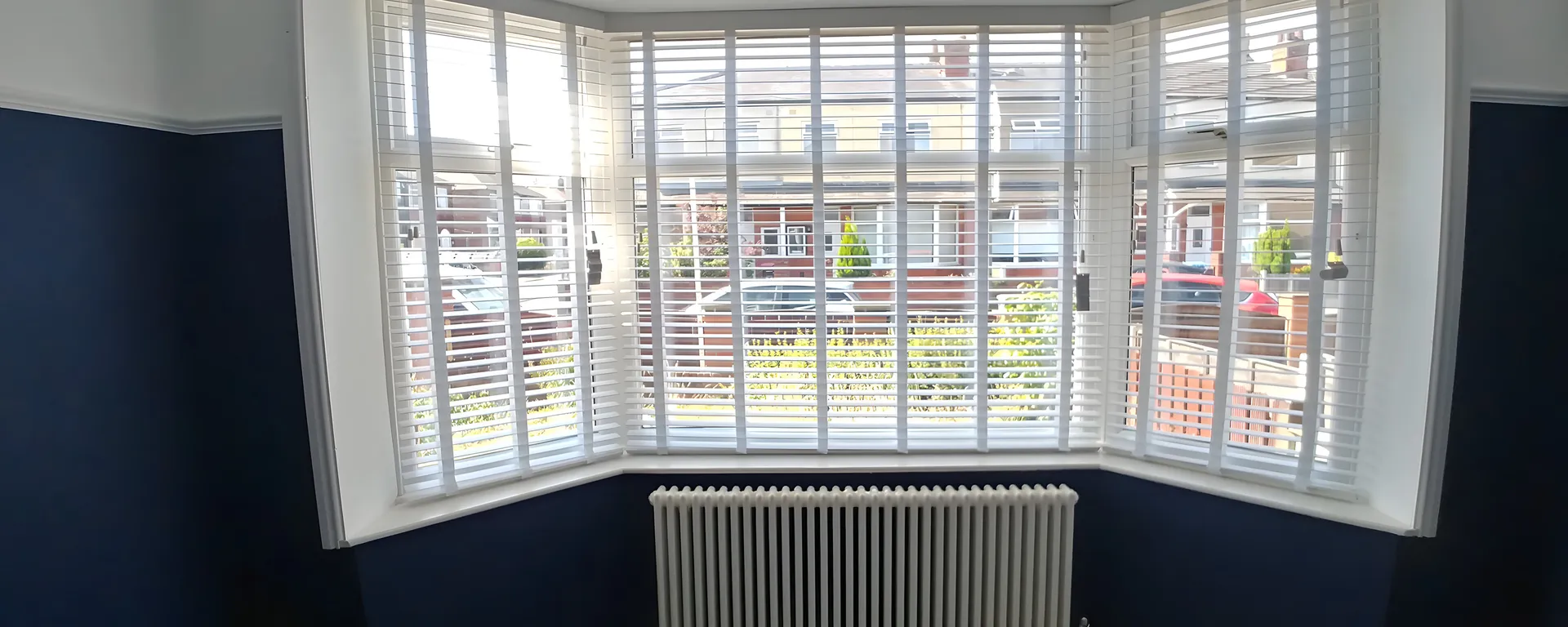 White wooden Venetian blinds fitted to every window of a bay above a navy dado and a radiator