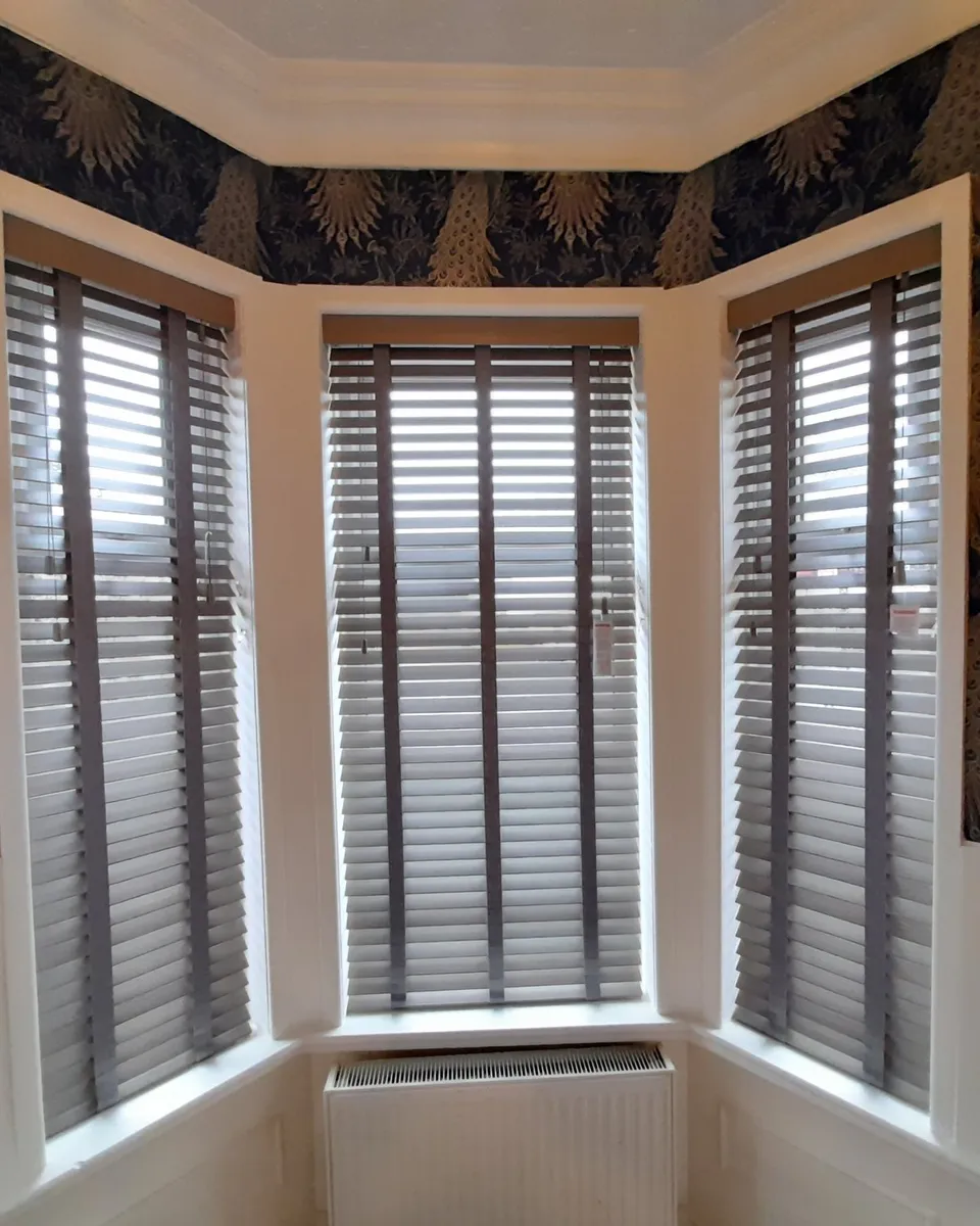 Wooden Venetian blinds fitted in each pane of a period bay window with deep cornicing, white panelling and navy peacock wallpaper