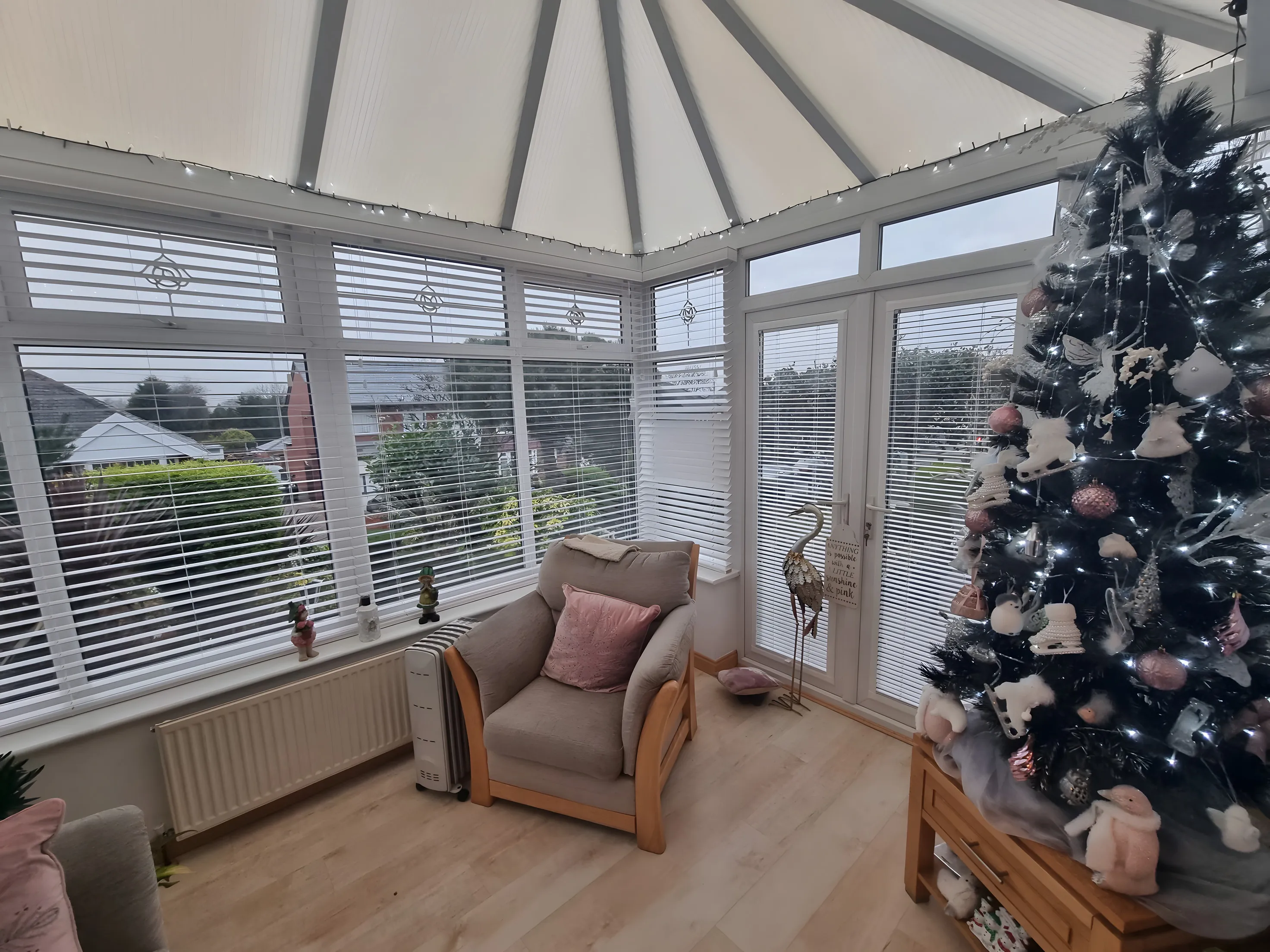 White Venetian blinds fitted to every window of a conservatory with an armchair and Christmas tree