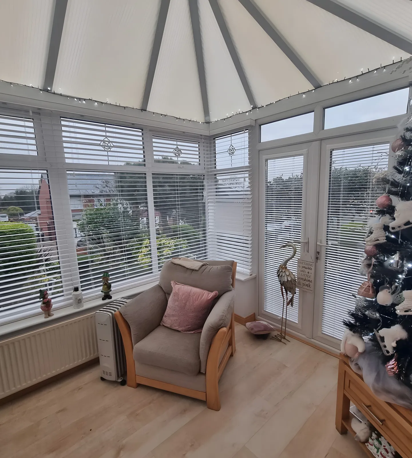 White Venetian blinds fitted to every window of a conservatory with an armchair and Christmas tree