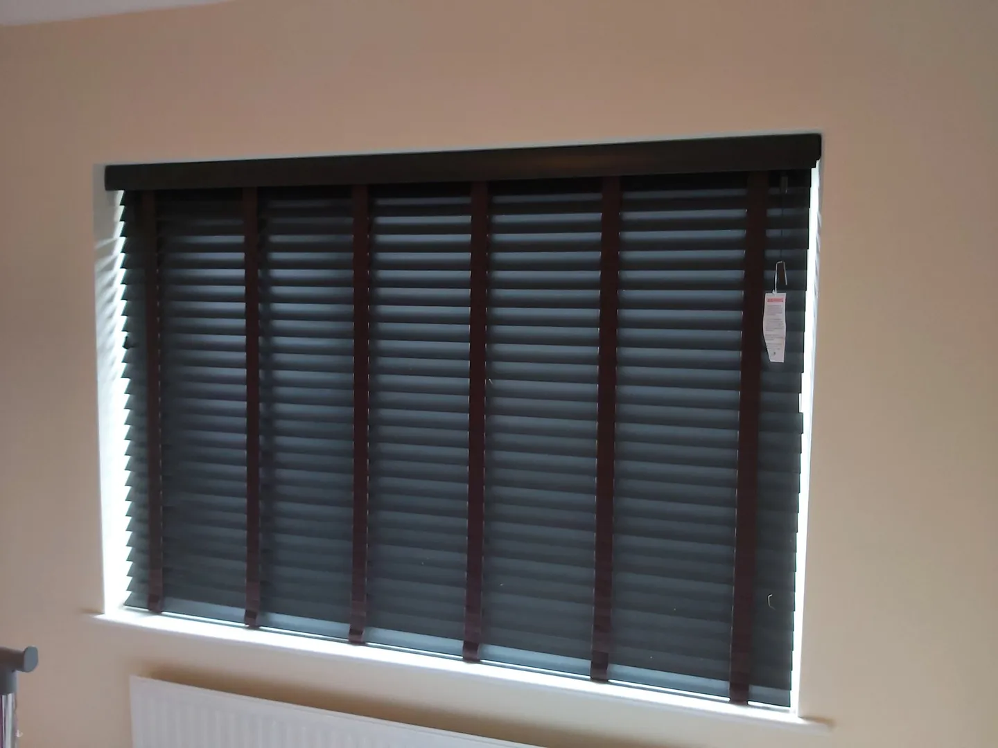 Dark wooden Venetian blind fitted to a bedroom window with the slats half open
