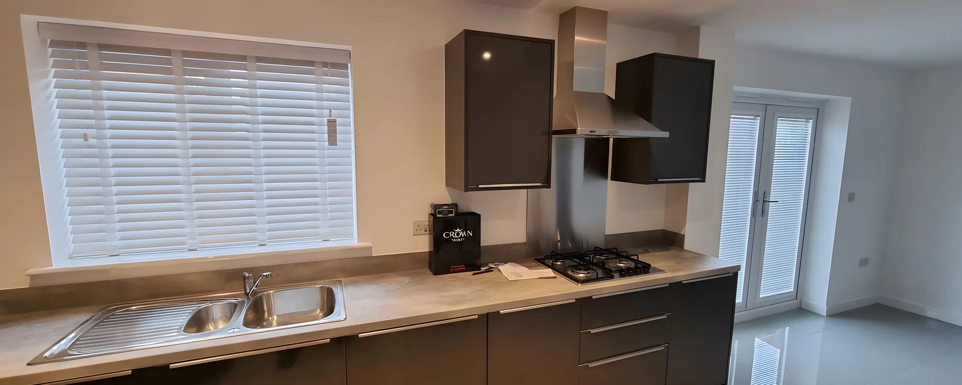White Venetian blinds fitted above the worktop of a grey handleless kitchen