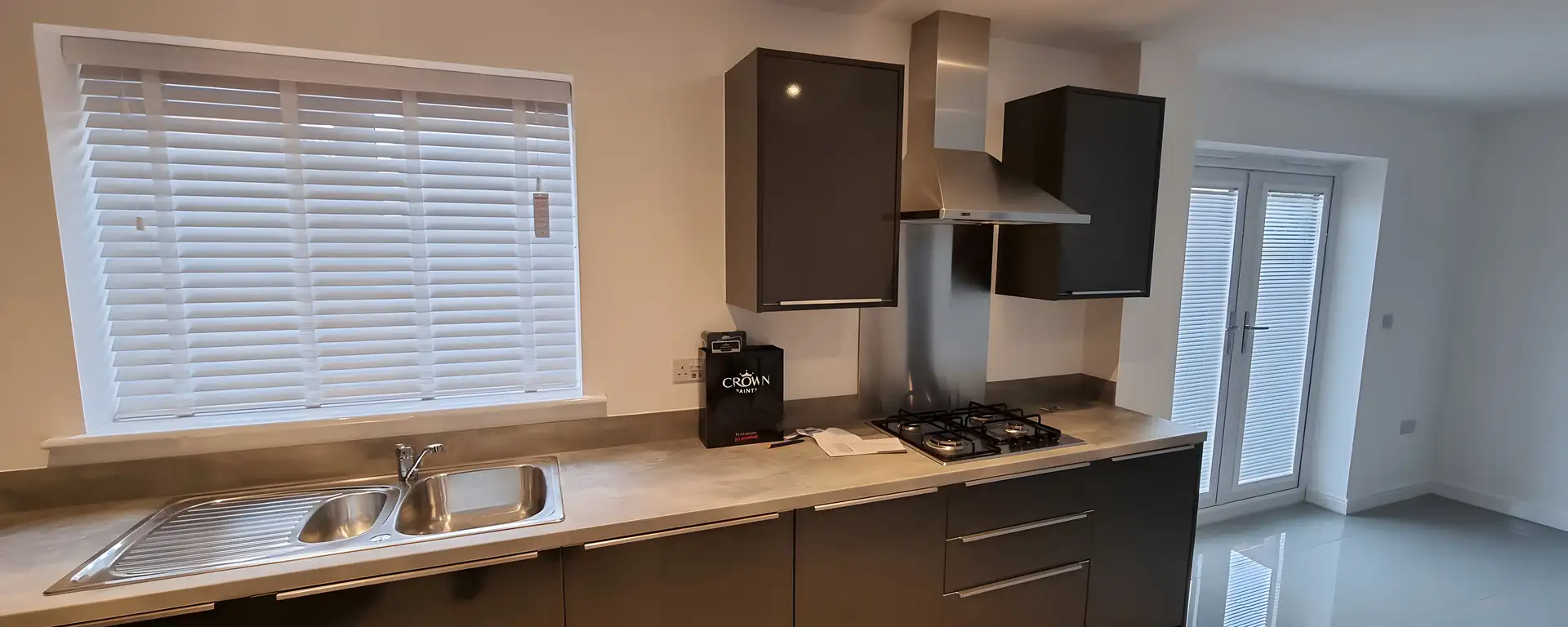 White Venetian blinds fitted above the worktop of a grey handleless kitchen