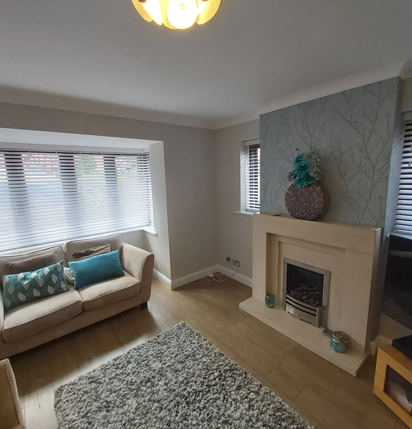 White Venetian blinds in a living room bay beside a fireplace and grey sofa