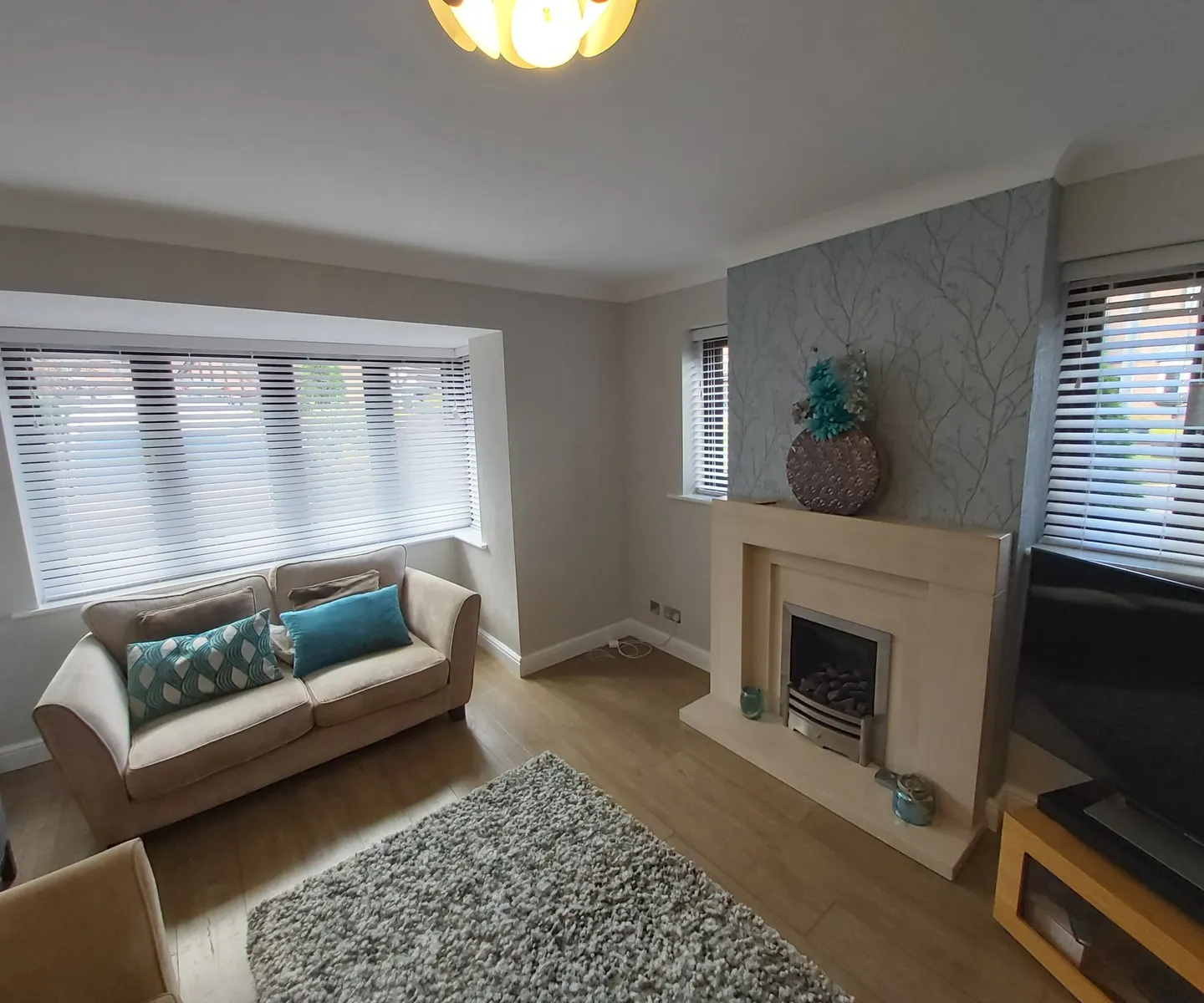 White Venetian blinds in a living room bay beside a fireplace and grey sofa