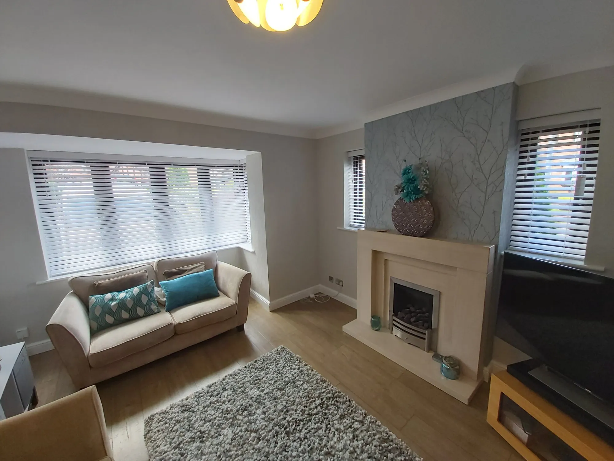 White Venetian blinds in a living room bay beside a fireplace and grey sofa