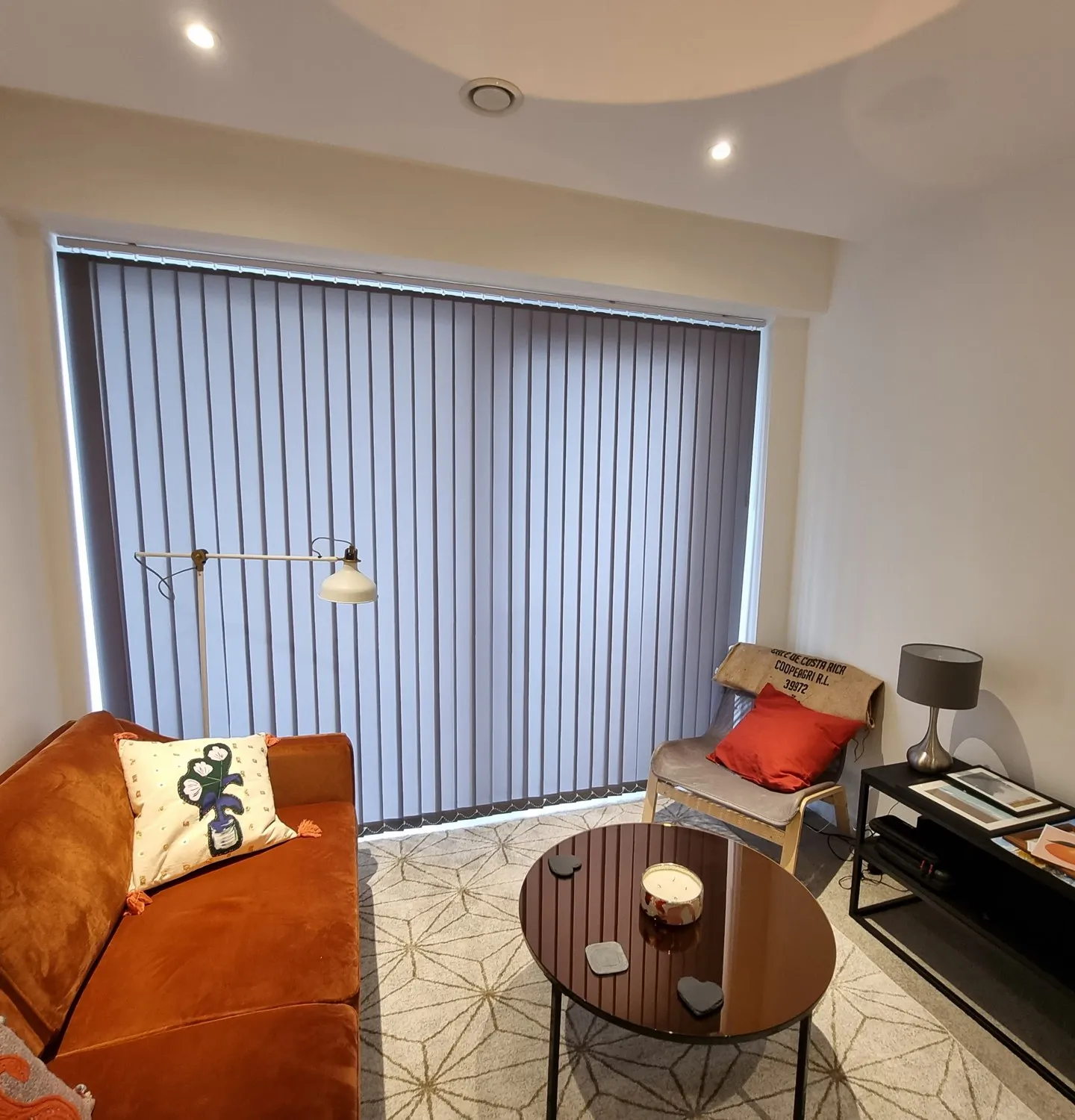 Grey vertical blinds on the balcony doors of an apartment with an orange velvet sofa