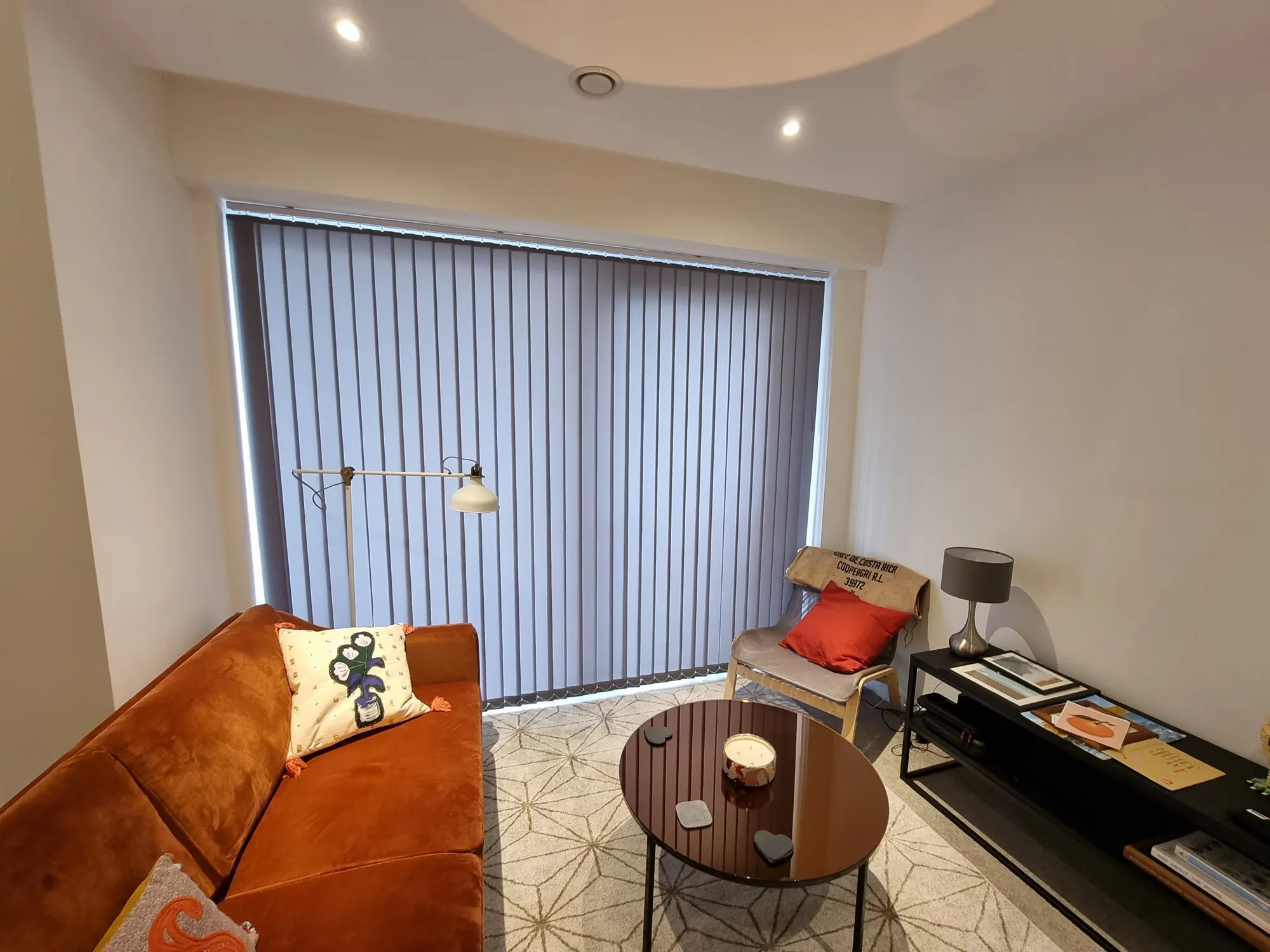 Grey vertical blinds on the balcony doors of an apartment with an orange velvet sofa