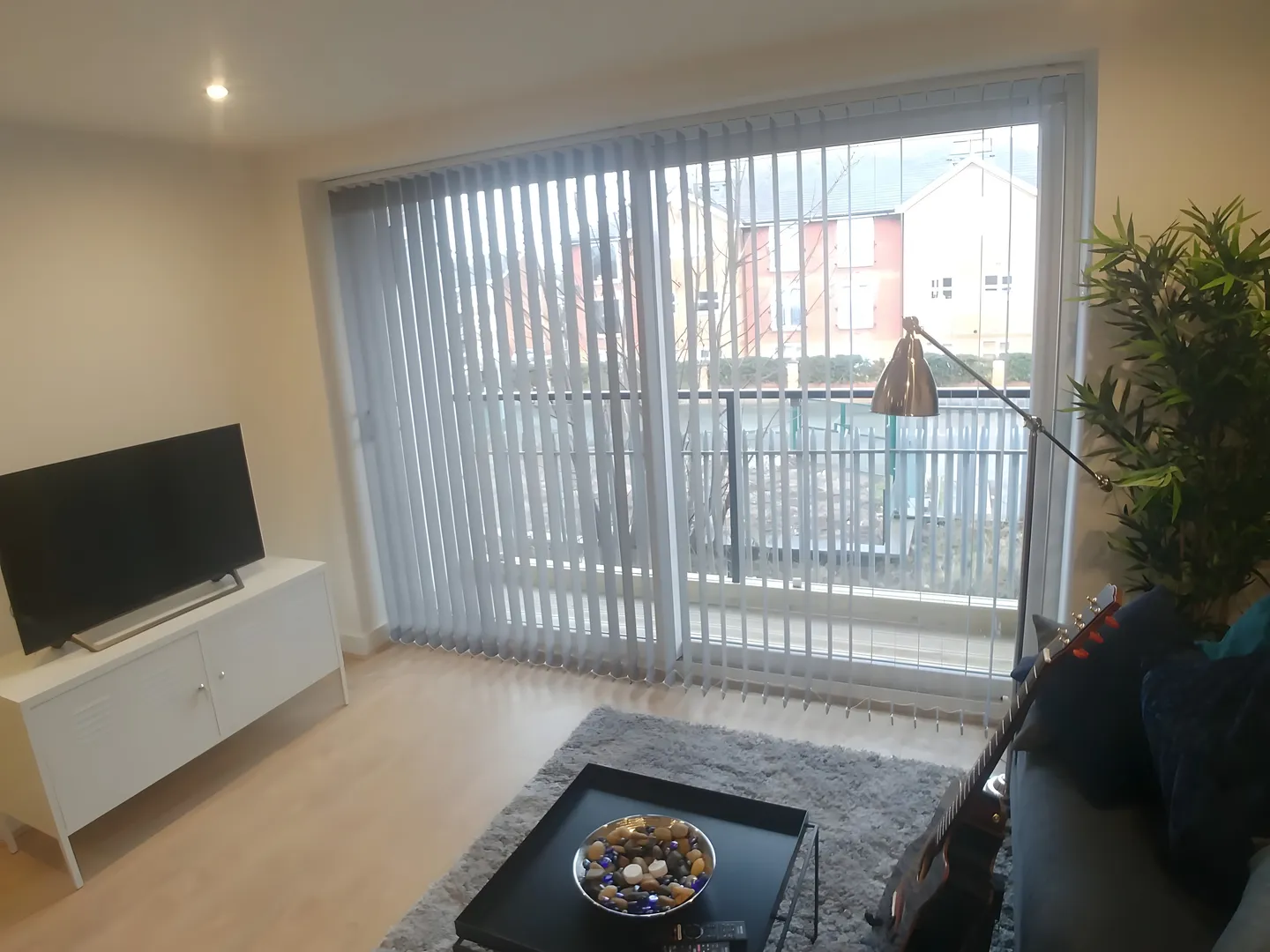 Vertical blinds across balcony doors in a living room with a television and plants