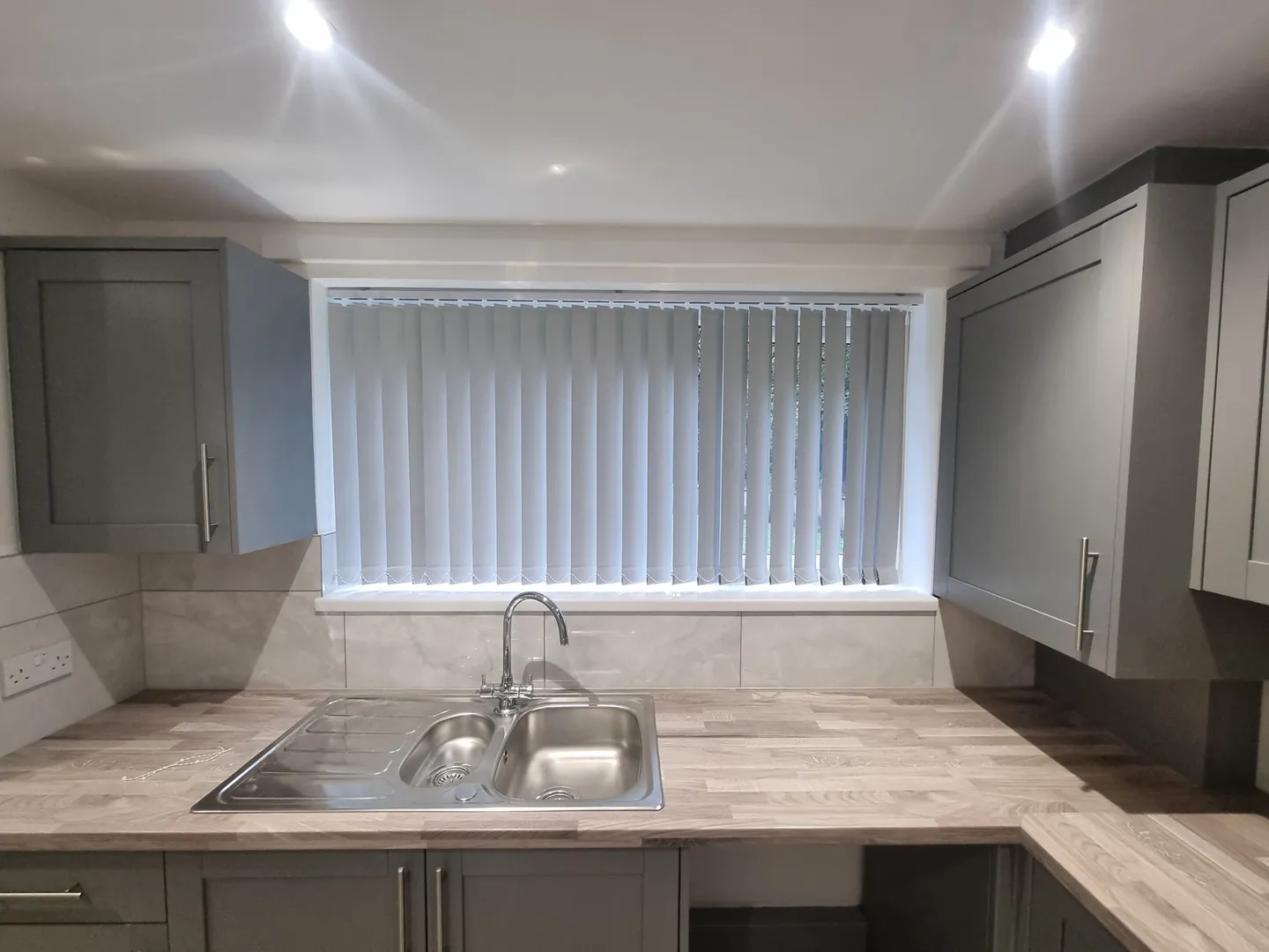 Cream vertical blinds at the window above a kitchen sink in a grey shaker kitchen