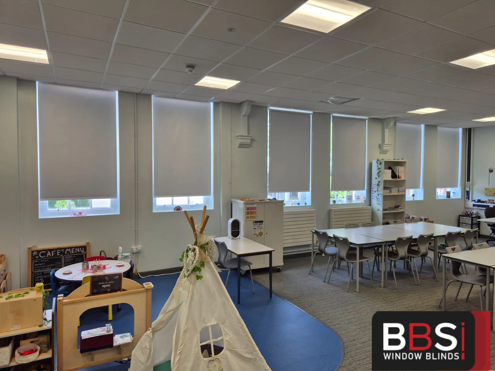 Childcare training room with five matching blackout roller blinds along the window wall behind the role play area